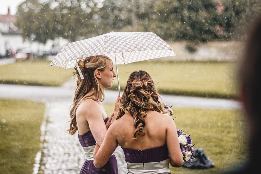 bridesmaids shelter from the rain under an umbrella