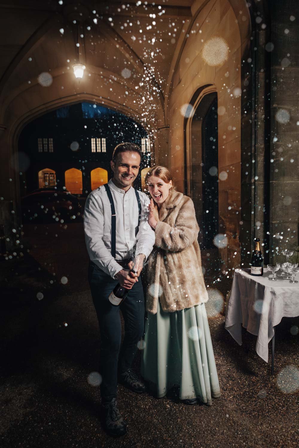 bride and groom spray champagne in from of stately home wedding venue