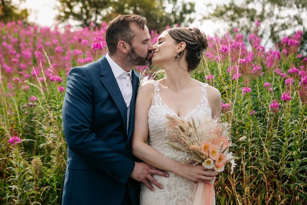 bride and groom kiss next to wildflowers at their countryside wedding
