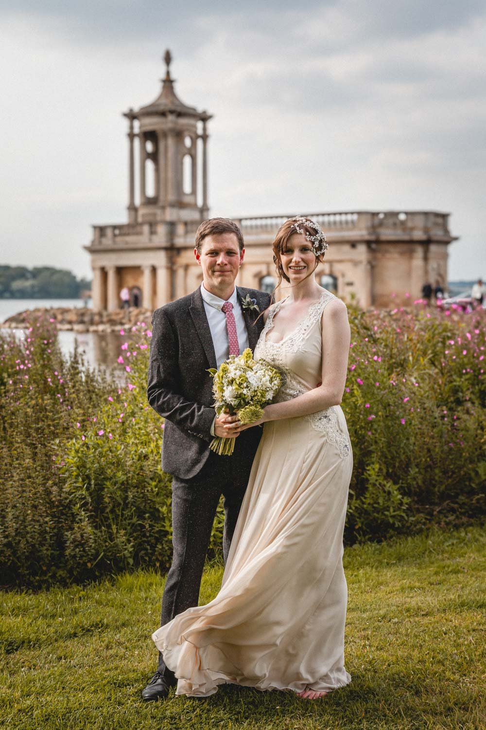 bride and groom smile in front of Normanton church at Rutland Water