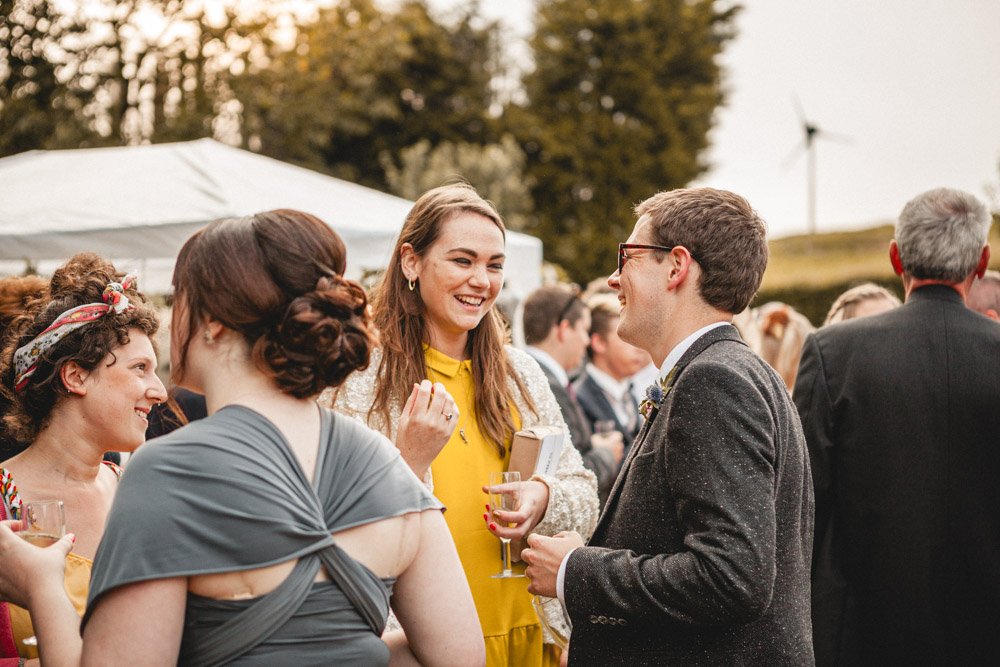 Groom smiles and laughs with a guest on a summer evening