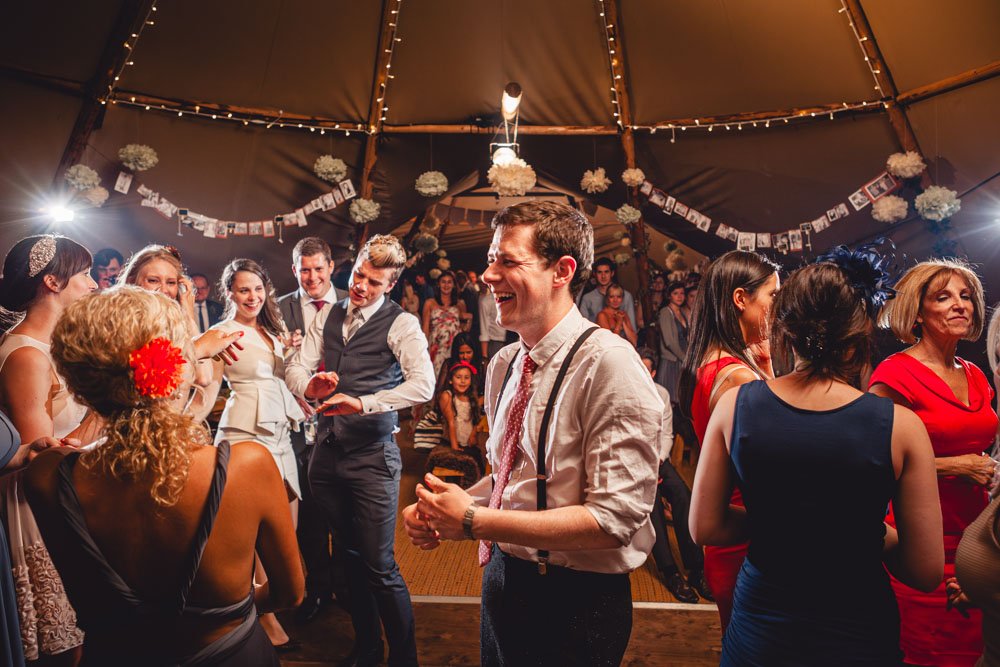 Groom surrounded by guests, smiling and dancing in a tipi wedding