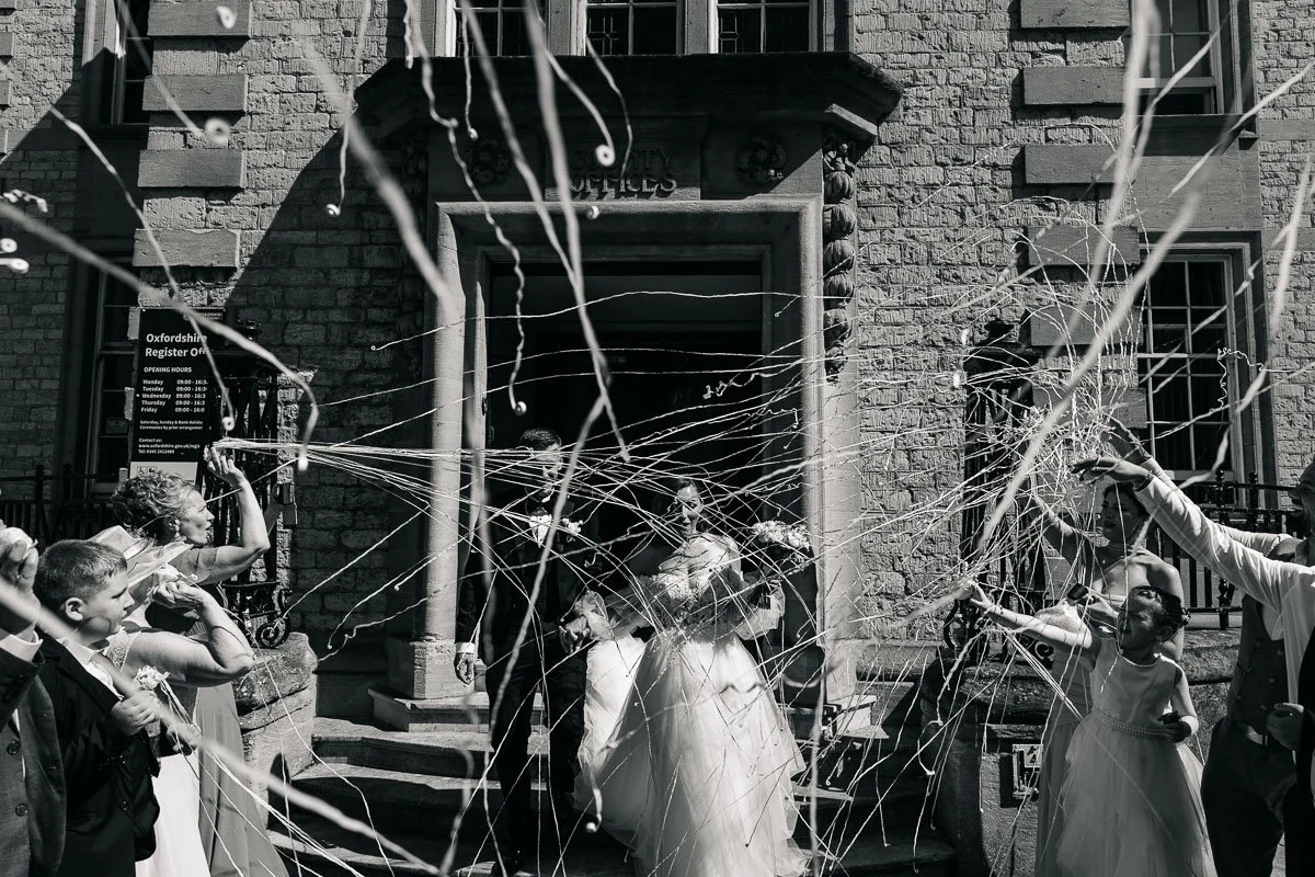 guests throw tethered confetti over a bride and groom on the steps outside oxford registry office
