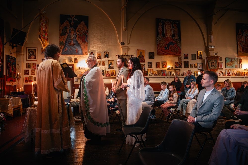 bride and groom stand with vicar at altar in an orthodox church wedding in Lincoln