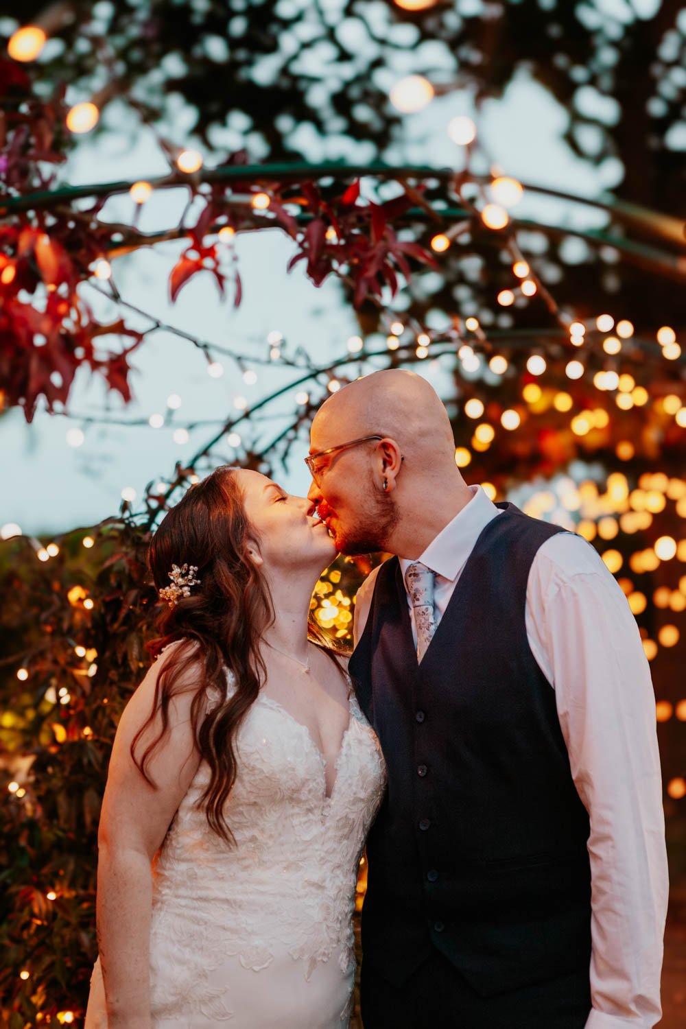 bride and groom kiss under fairy lights in a garden