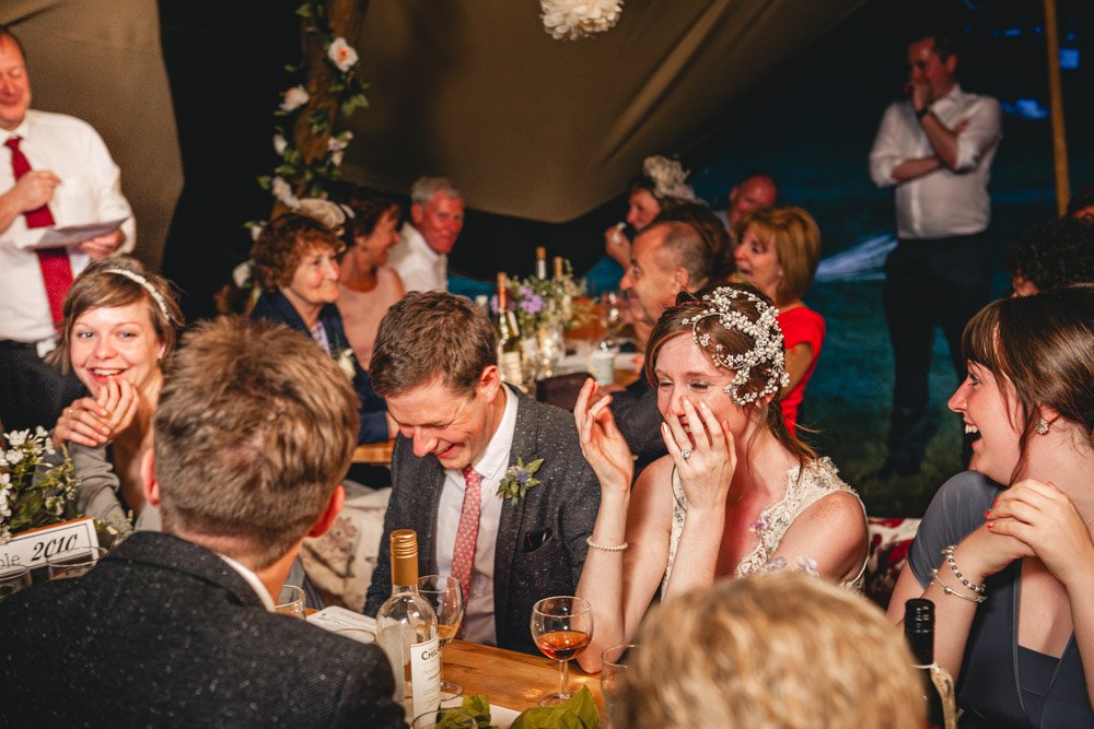 bride and groom laugh hysterically as father makes wedding speech
