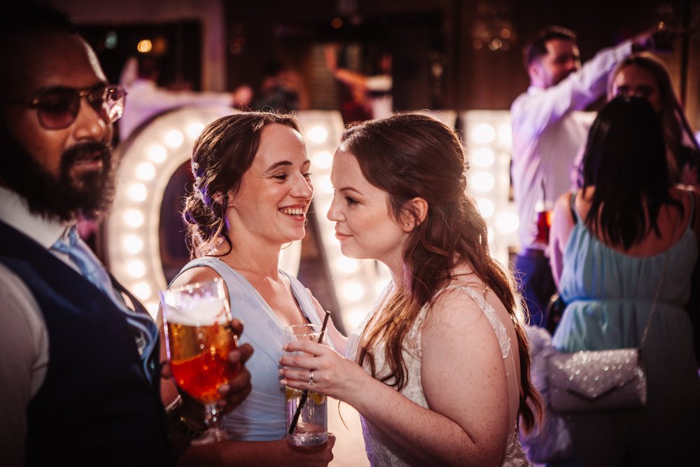 bridesmaid whispers in bride's ear on the dancefloor