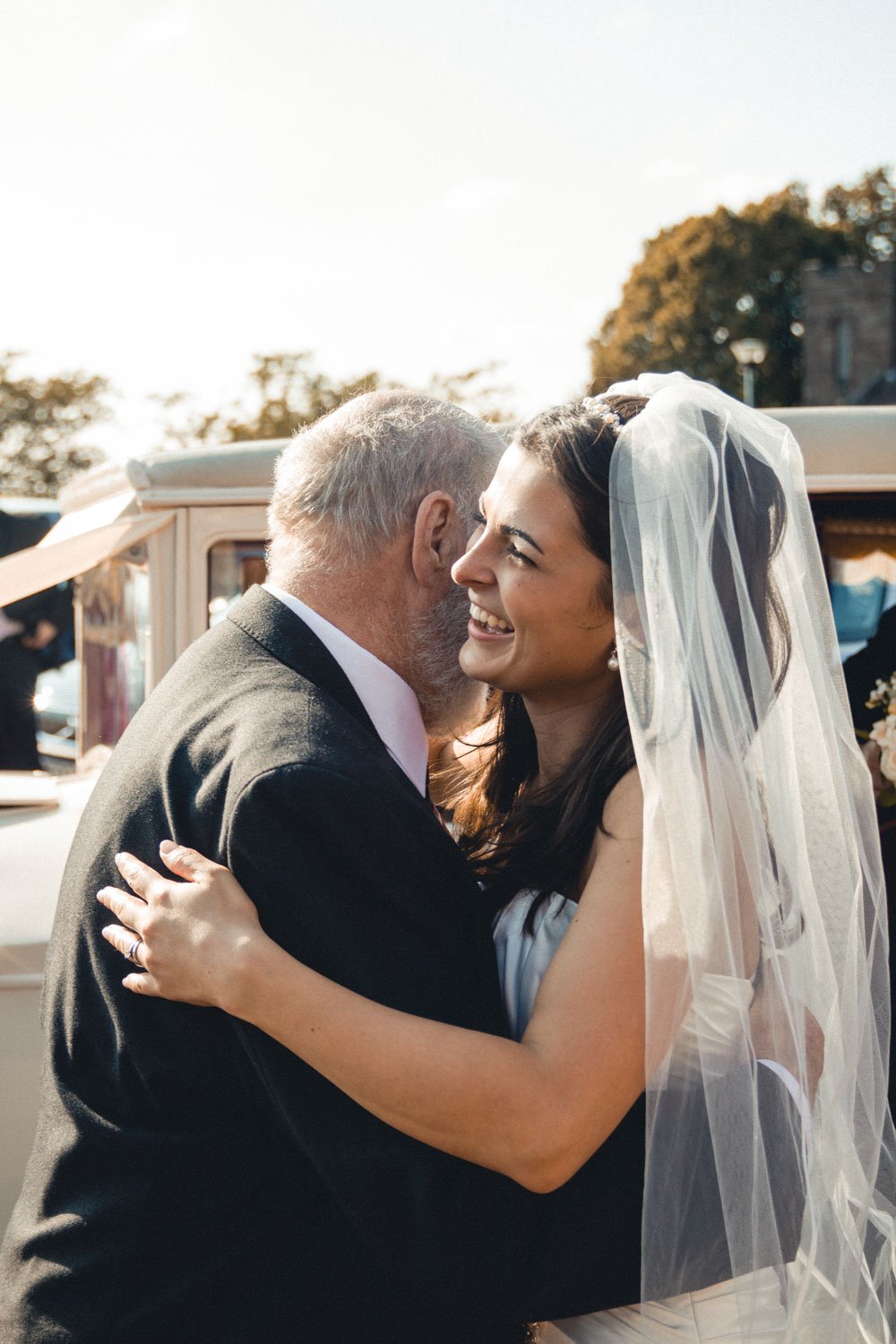 Bride hugs grandfather next to classic Rolls Royce car