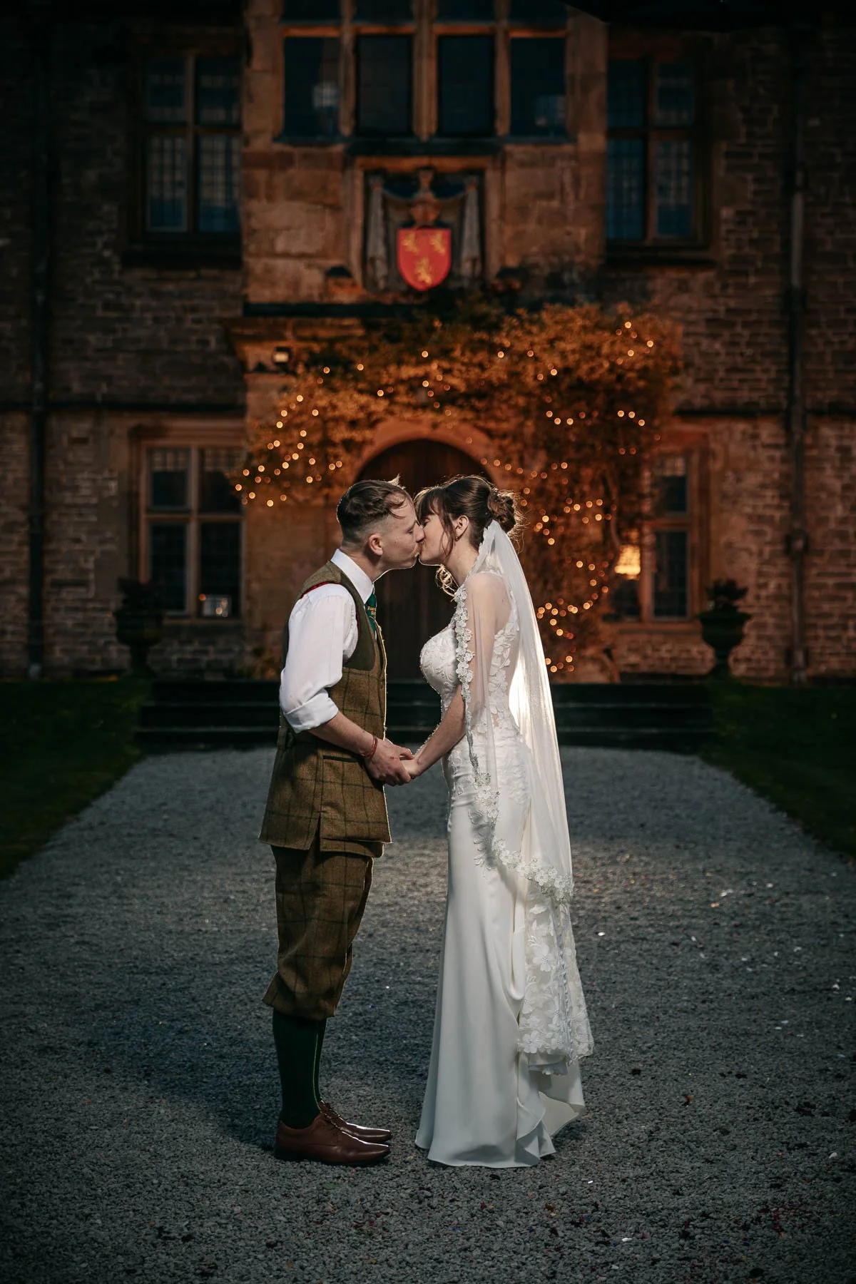 bride and groom kiss in front of Tissington Hall at night