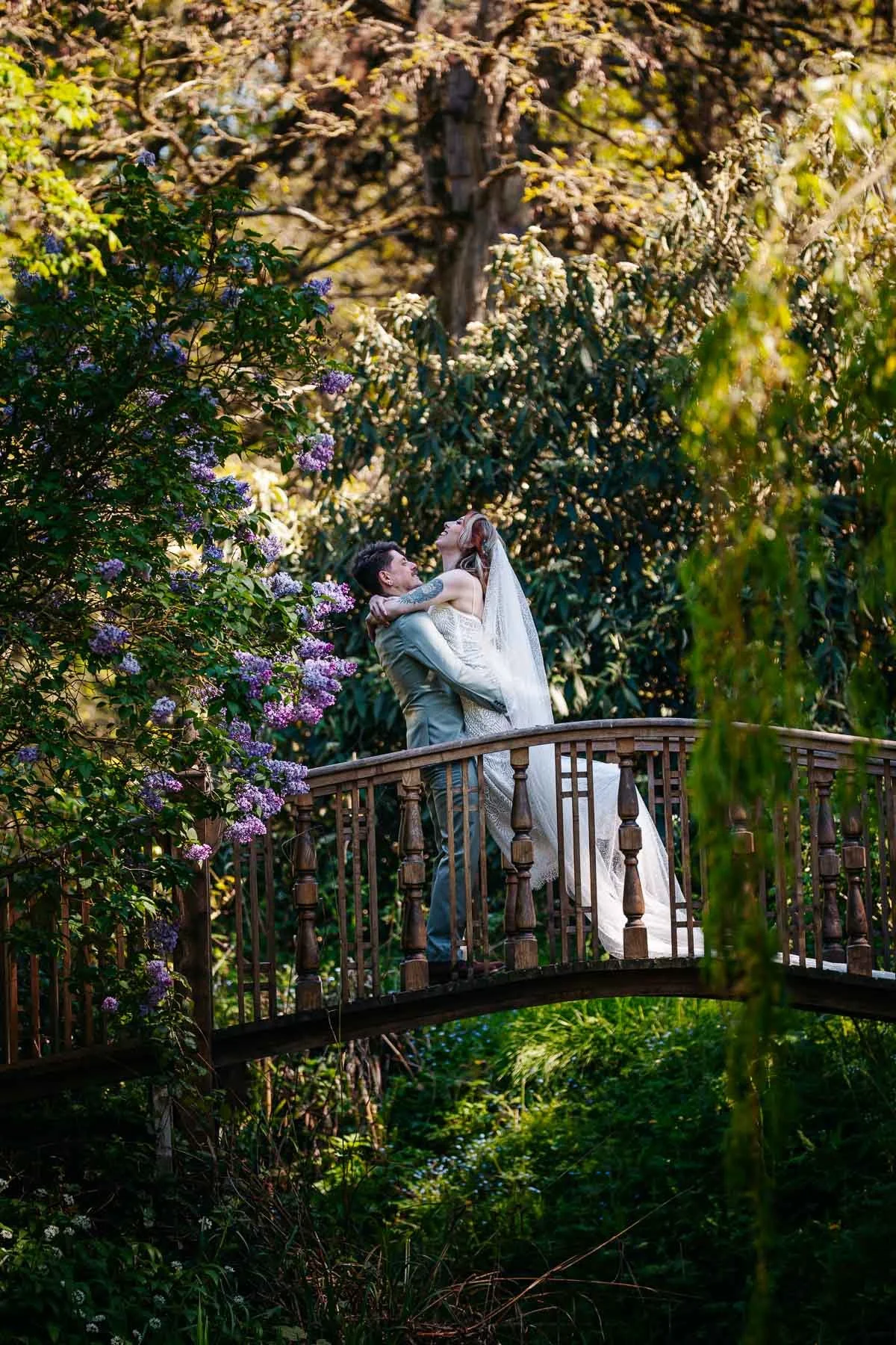 groom holds his bride on a bridge in the gardens at Whatton House