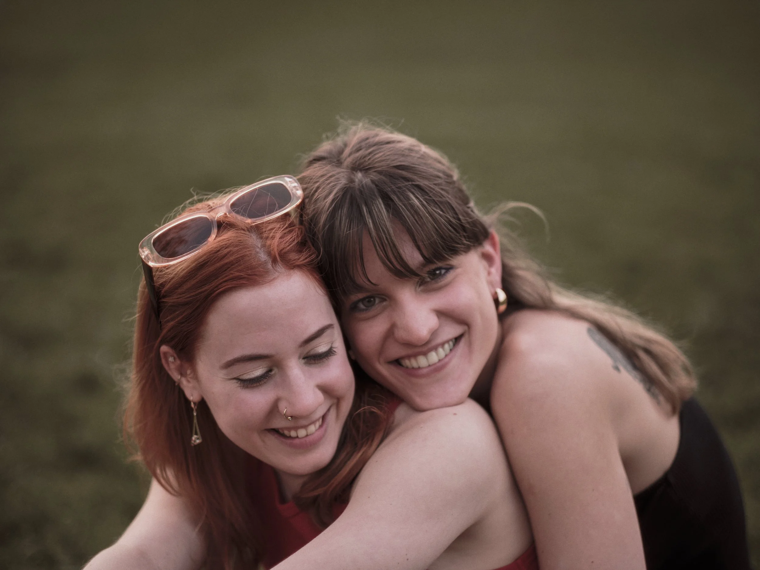 Two women hugging each other outdoors, smiling, with a blurred green background.