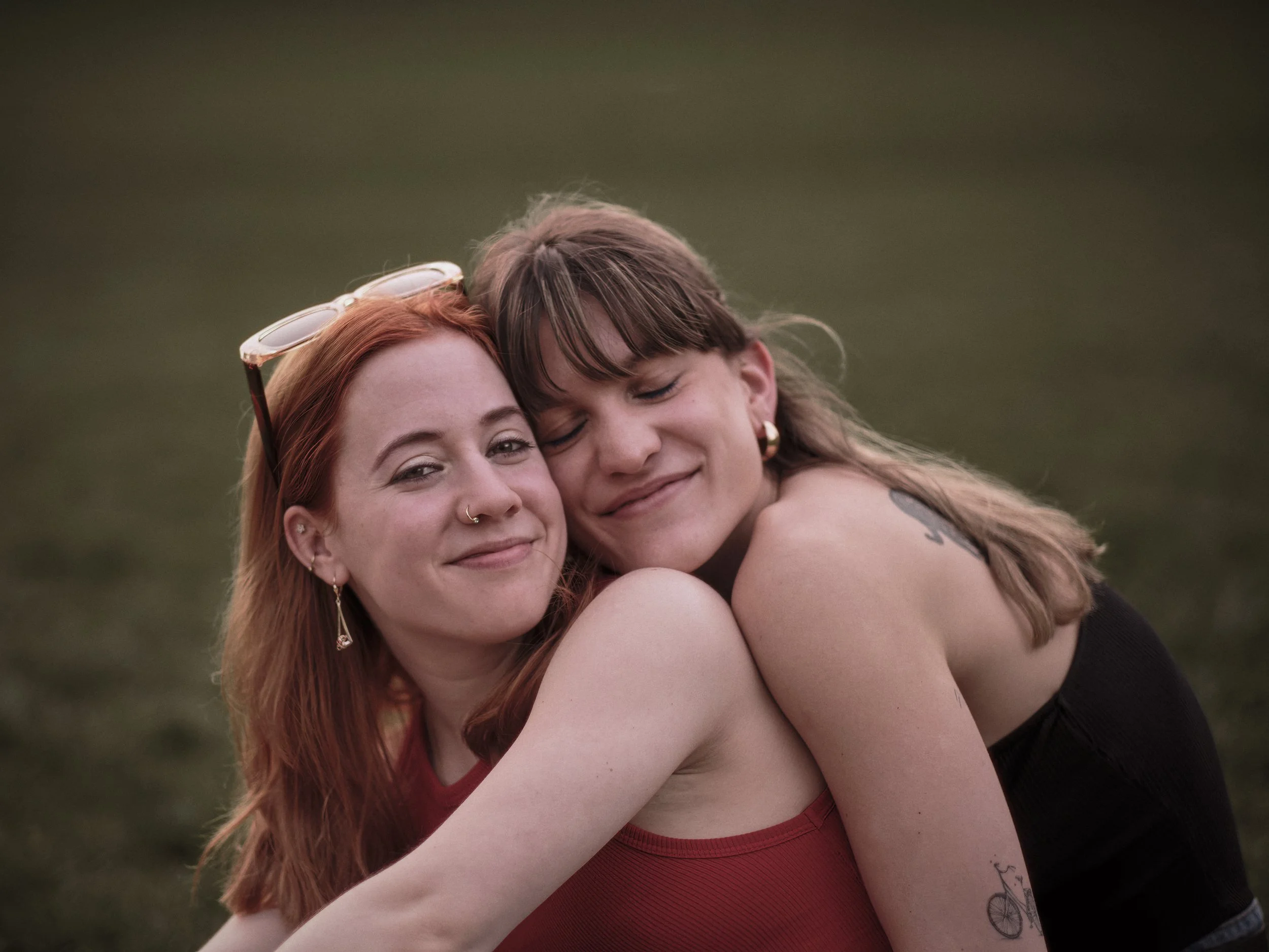 Two women hugging and smiling outdoors with a blurred green background.