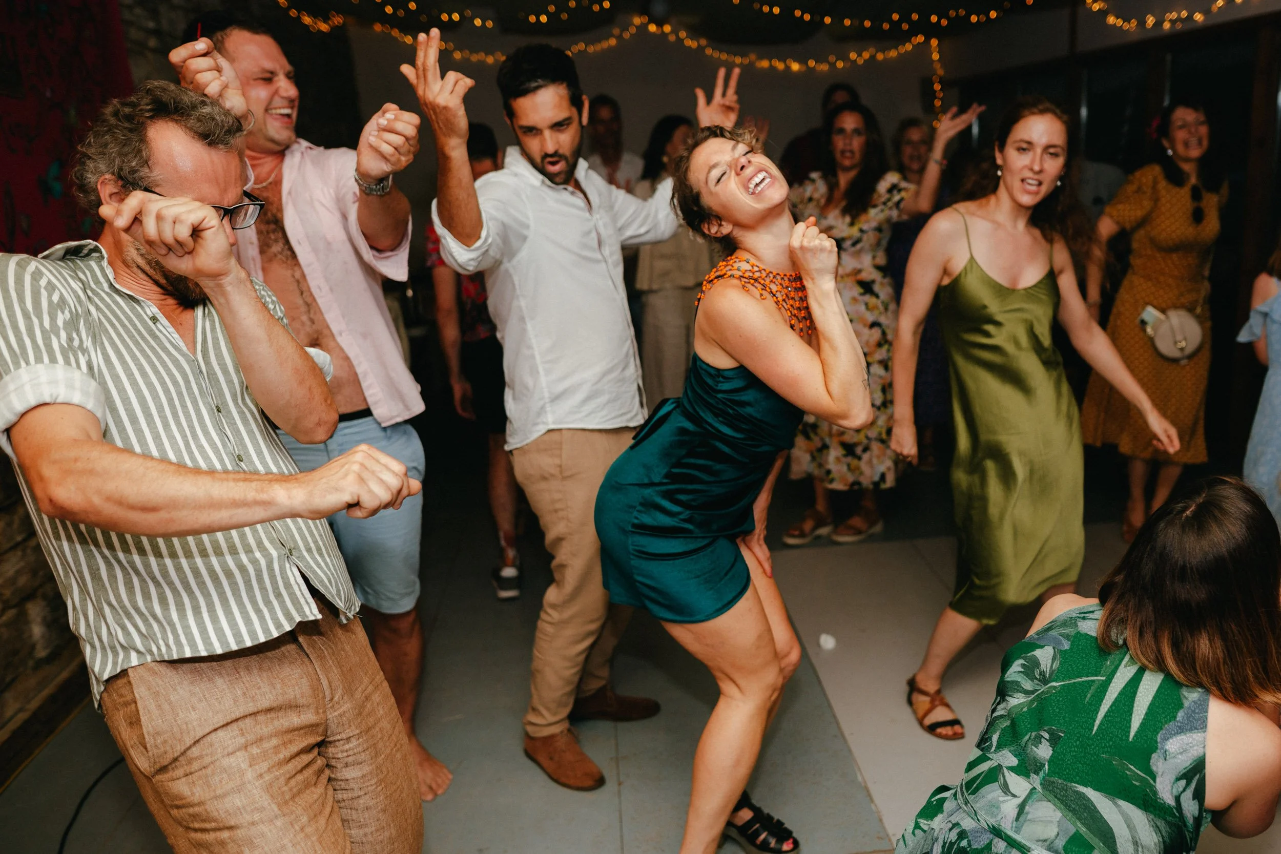 People dancing enthusiastically at a party with string lights overhead.