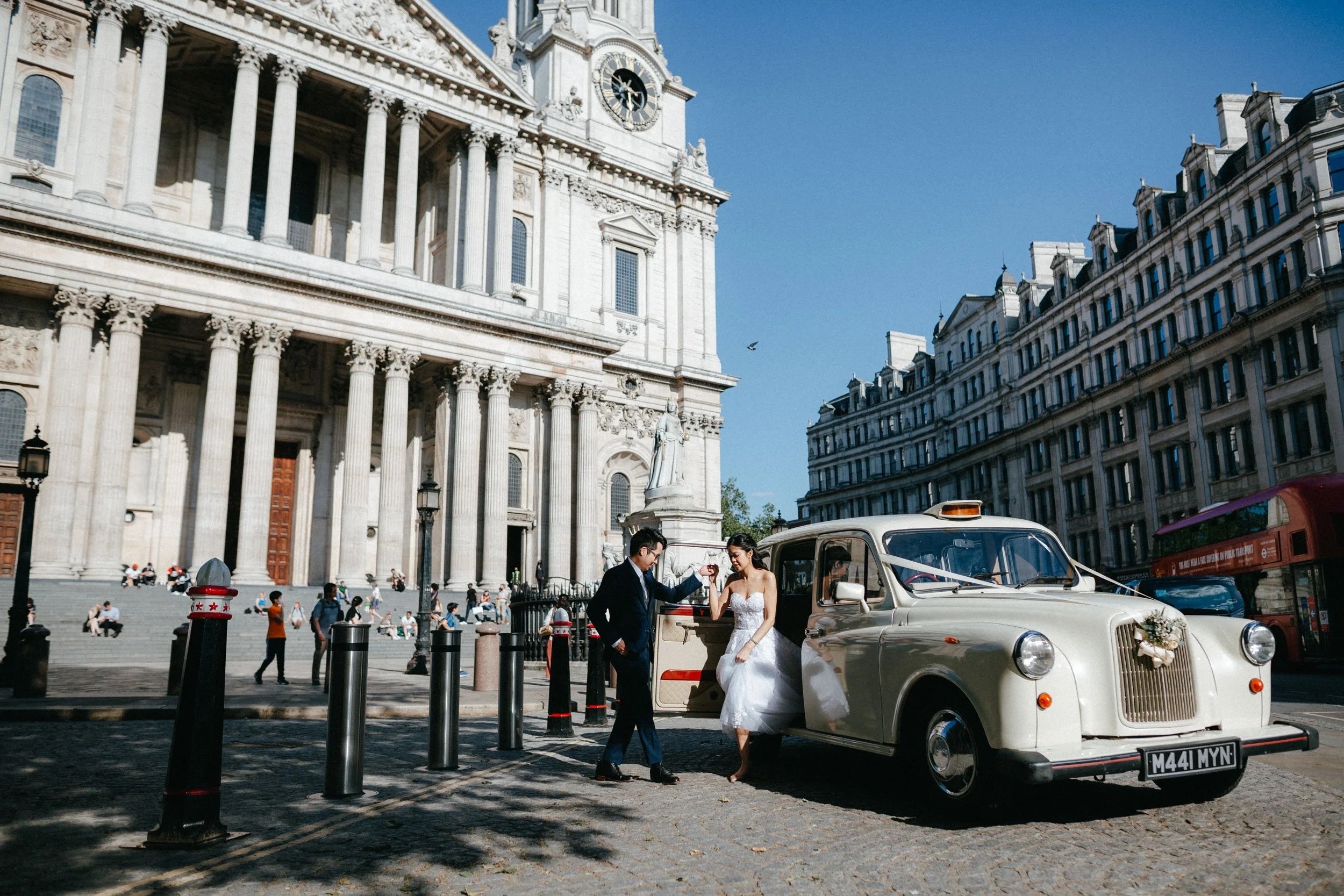 Bride and groom outside St. Paul's Cathedral in London with a vintage taxi.