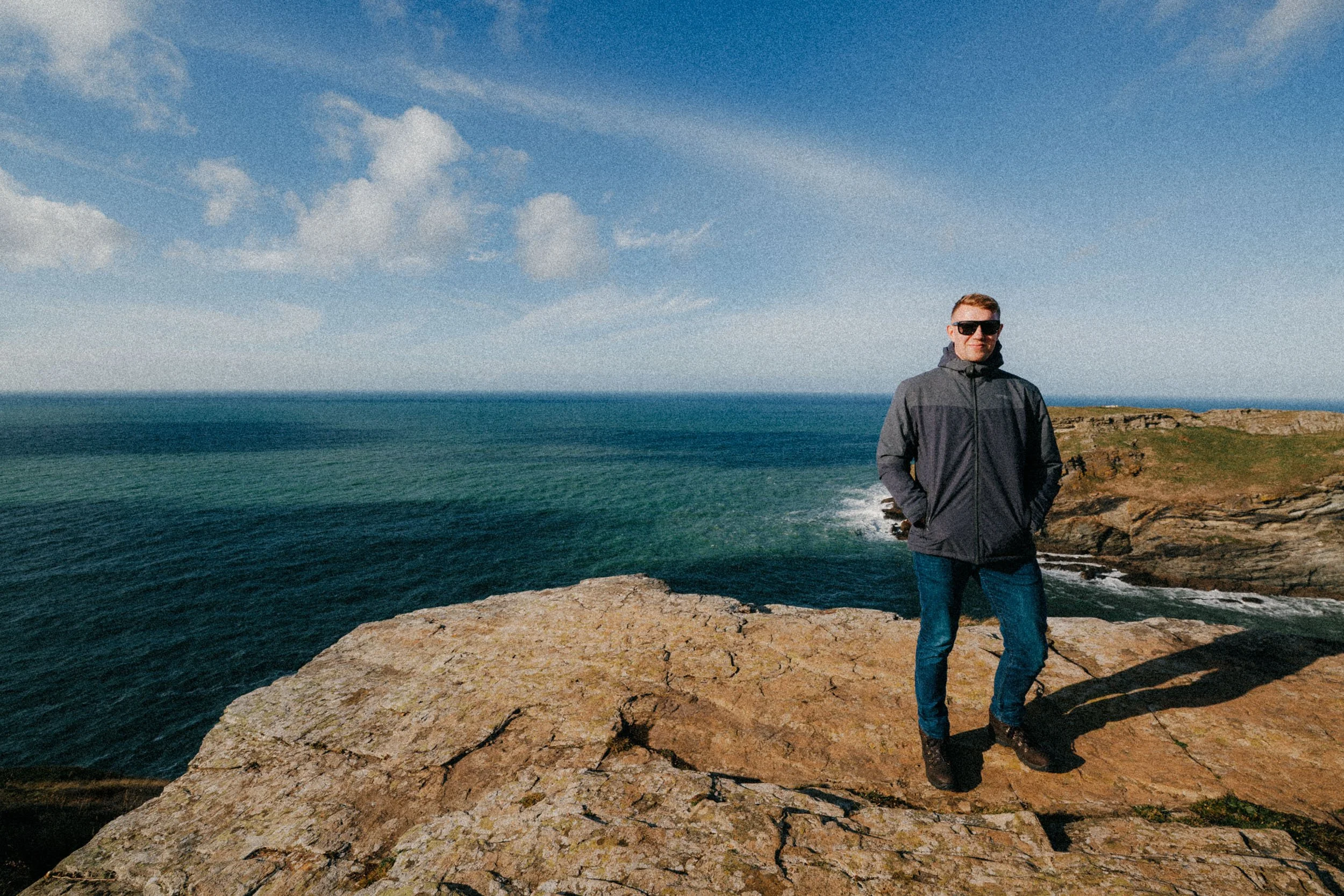 Man in jacket standing on rocky cliff overlooking ocean