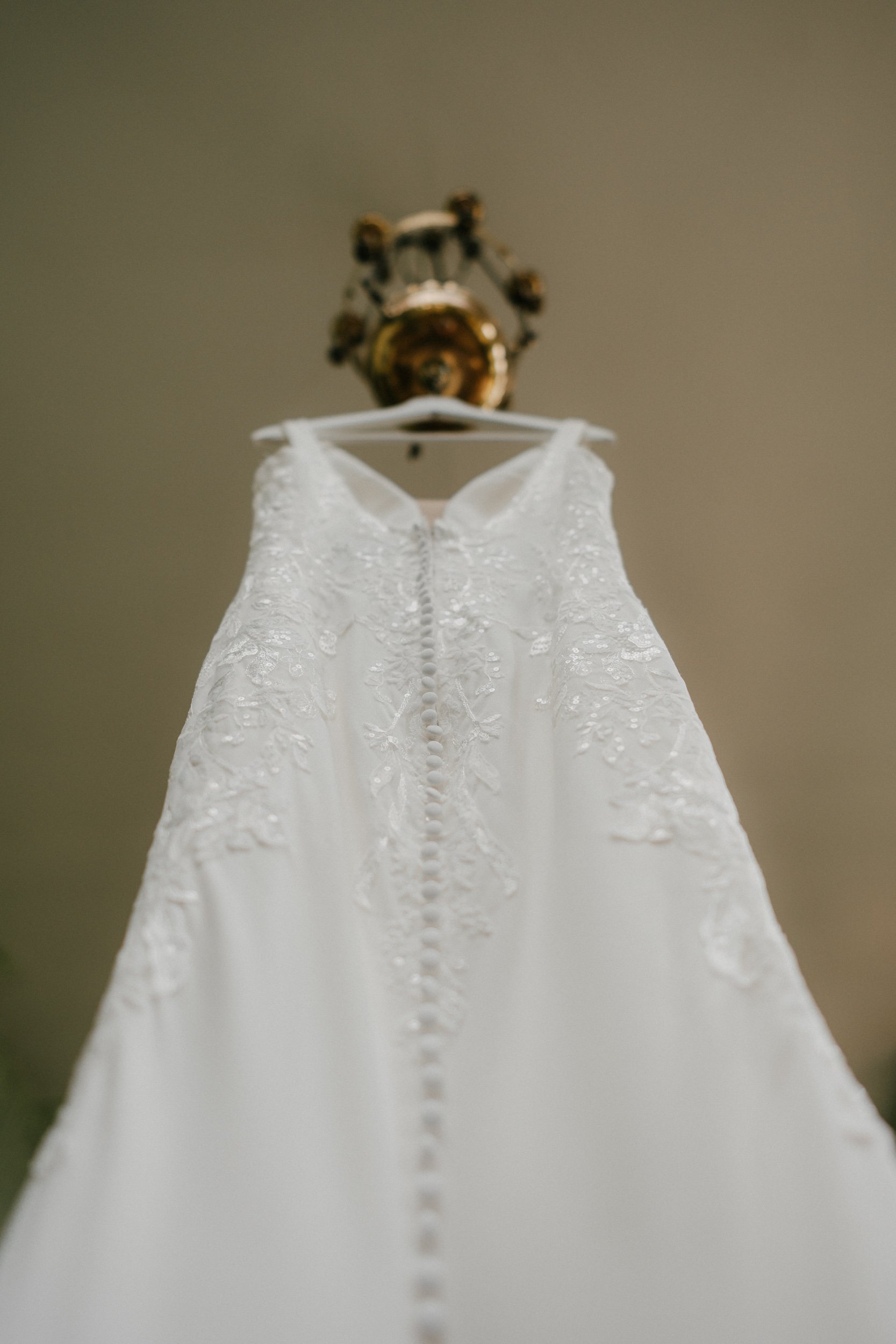 Close-up of a white wedding dress with lace details and buttons on a hanger.