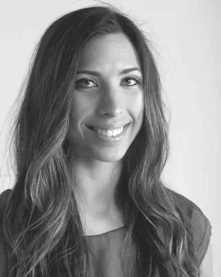 A smiling woman with long, wavy hair in a black and white photo.