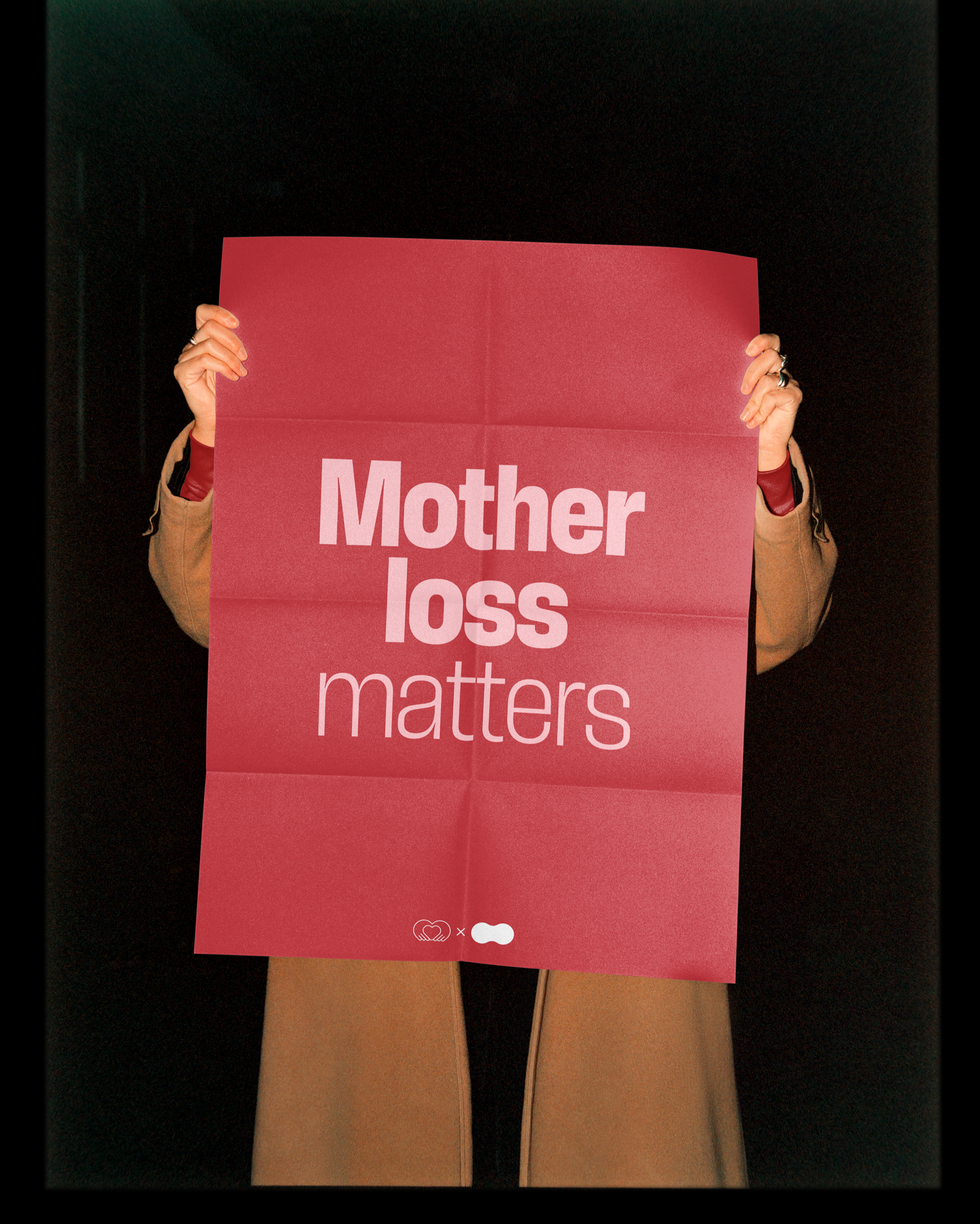 Person holding a pink sign that reads 'Mother loss matters' against a black background.