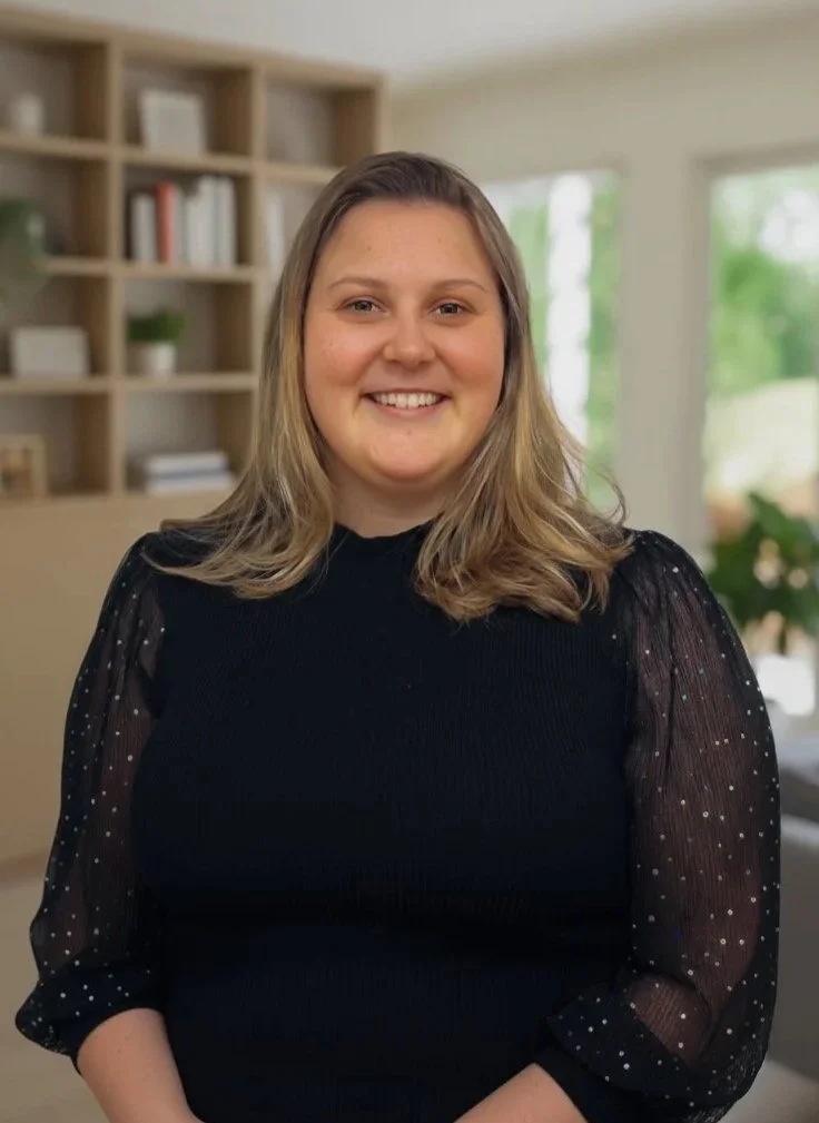 Smiling person in a black top with sparkly sleeves, indoors, blurred background.