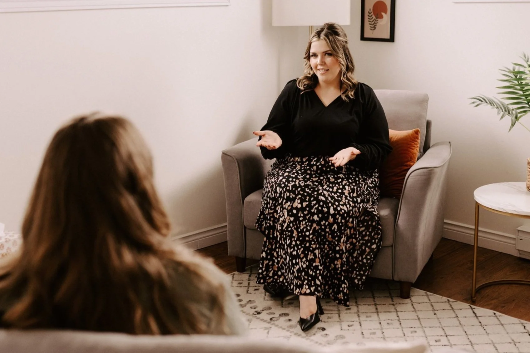 A woman sitting on a couch, talking to another person in a living room.