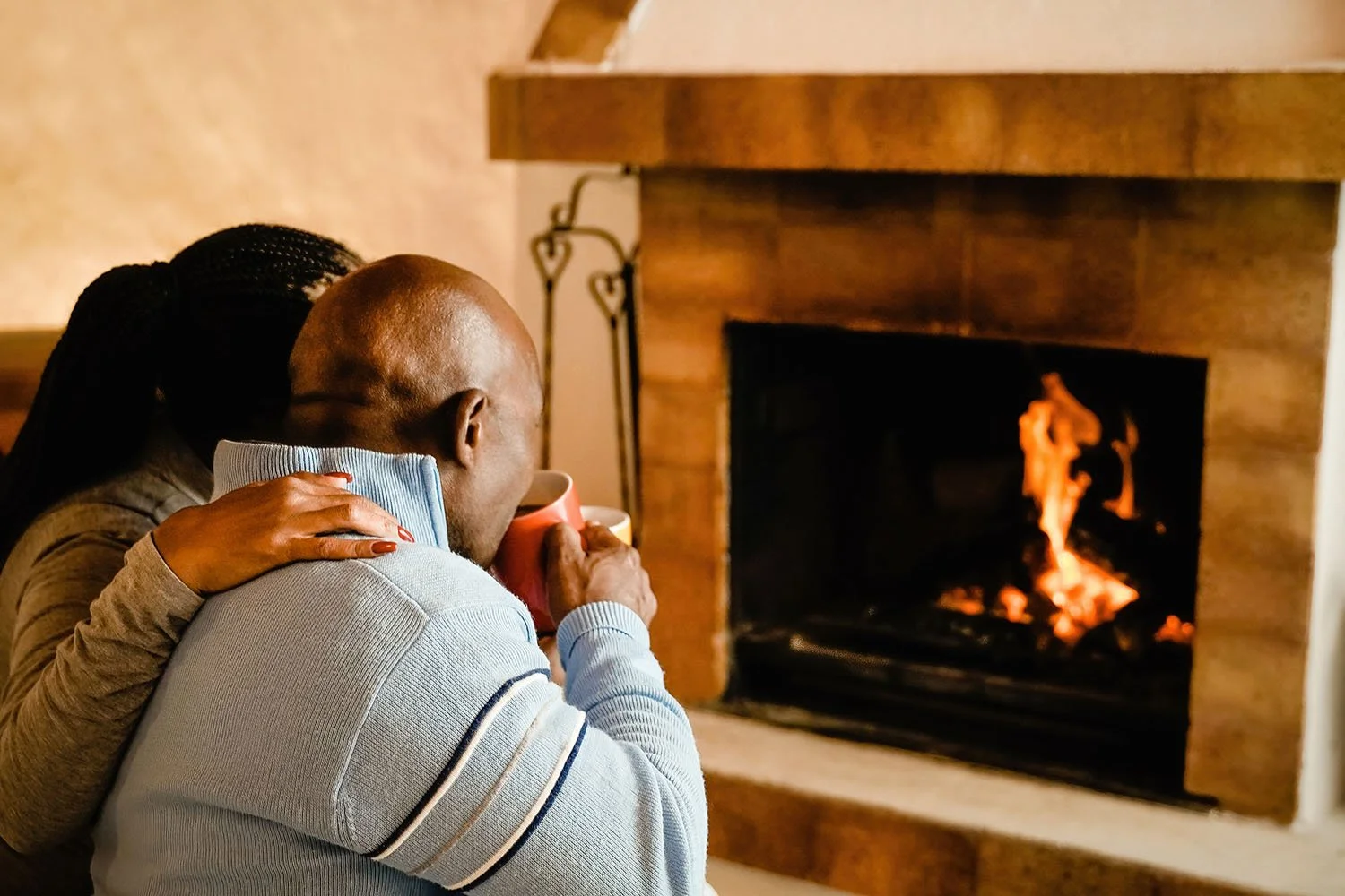 A couple hugging while sitting in front of a lit fireplace.