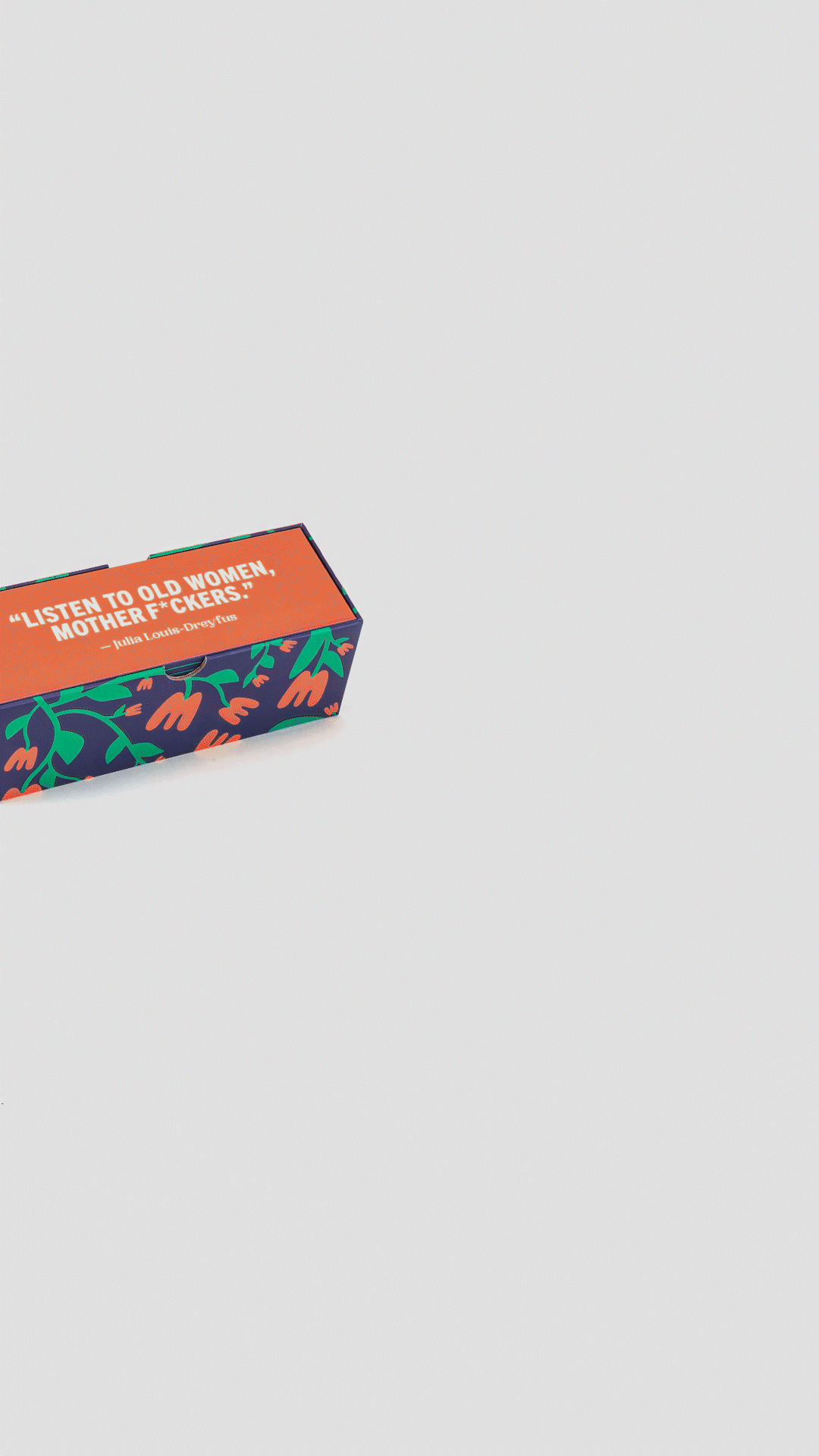 A rectangular box with colorful floral and leaf patterns features a quote in white text on an orange background that says, 'LISTEN TO OLD WOMEN, MOTHER F* CKERS!' — Julia Louis-Dreyfus. CADDIS brand glasses pop out of the packaging.