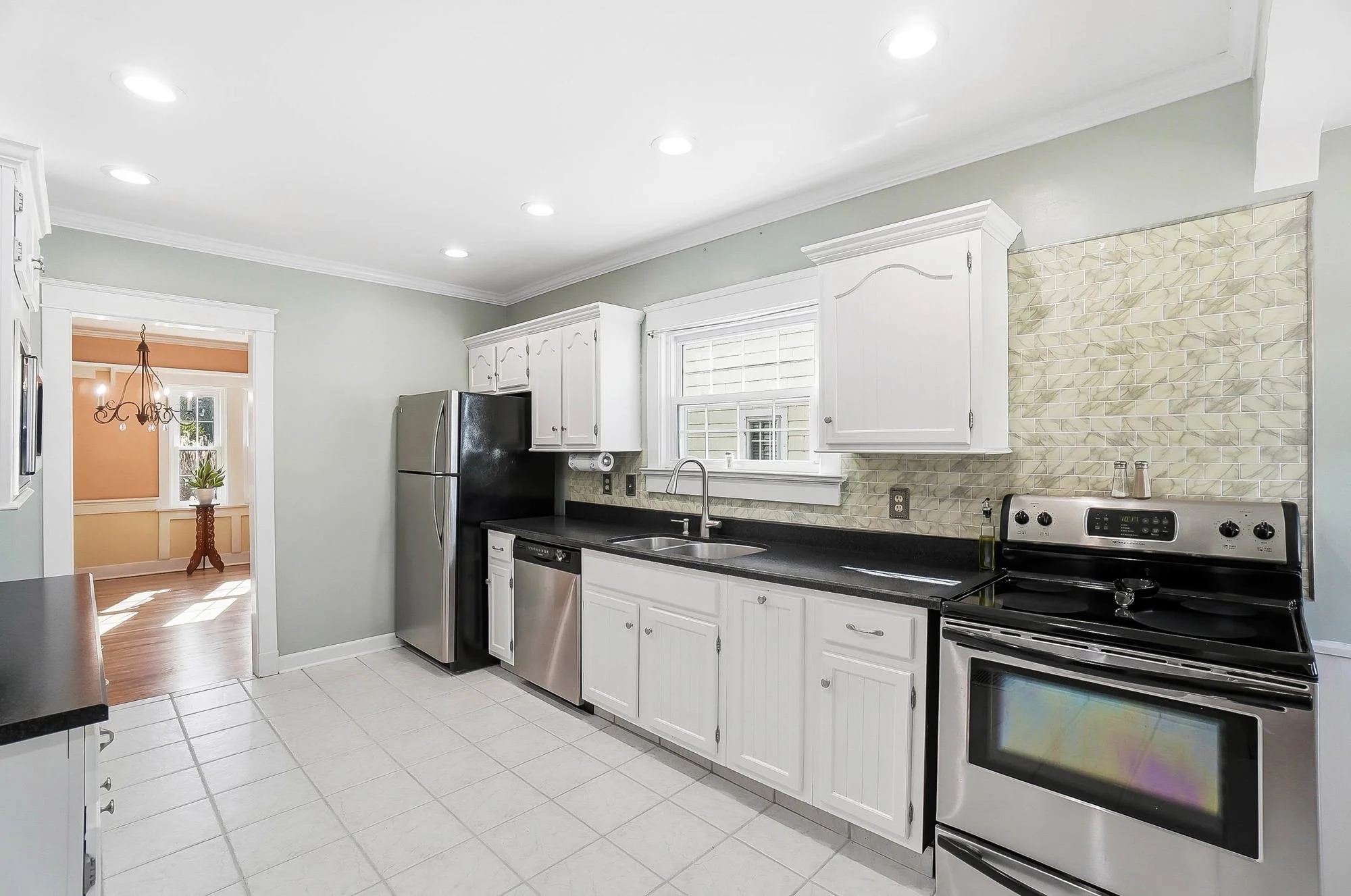 Kitchen with white cabinets, black countertops, stainless steel appliances, and a window above the sink