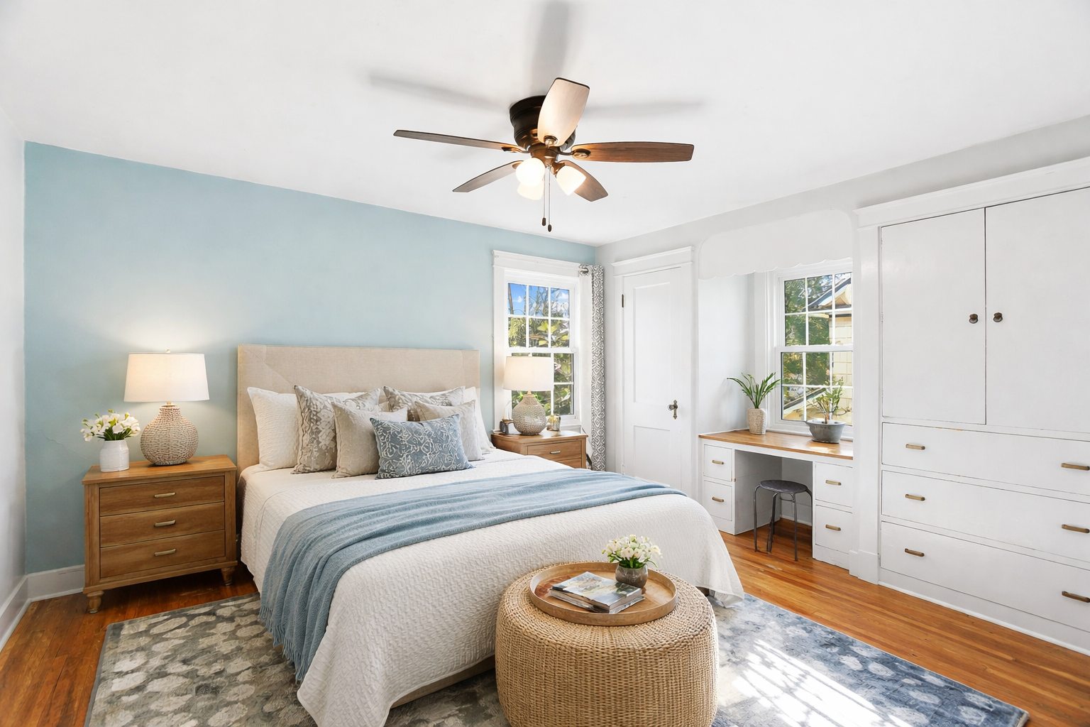 Bright bedroom with a white bed, wooden nightstands, blue accents, and natural light from two windows.