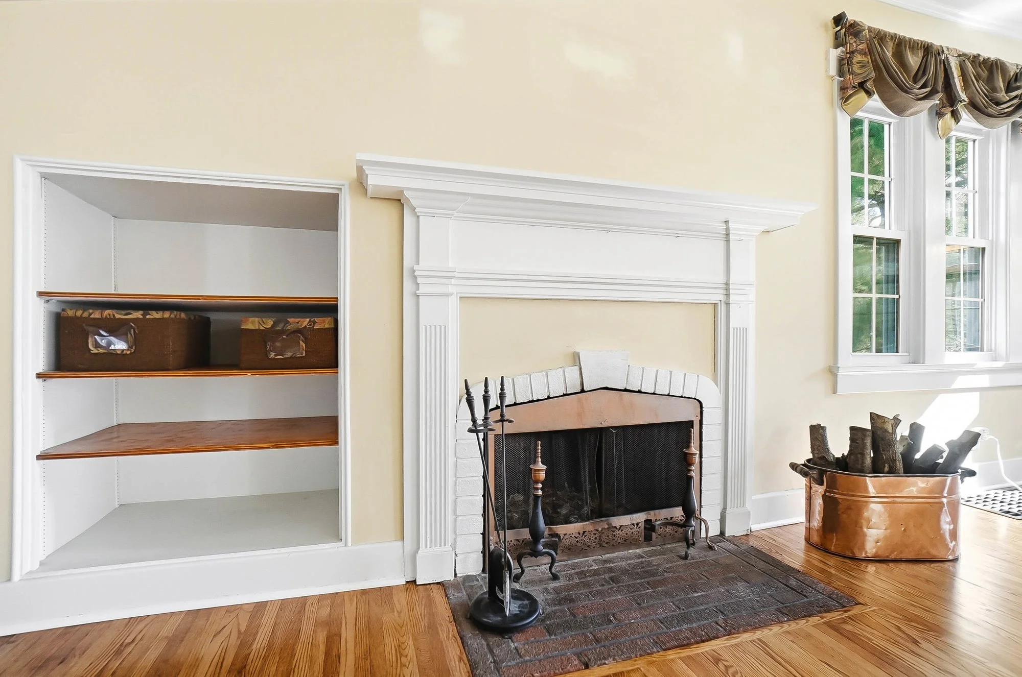 Living room with fireplace, built-in shelf, hardwood floor, and a window with draped curtains