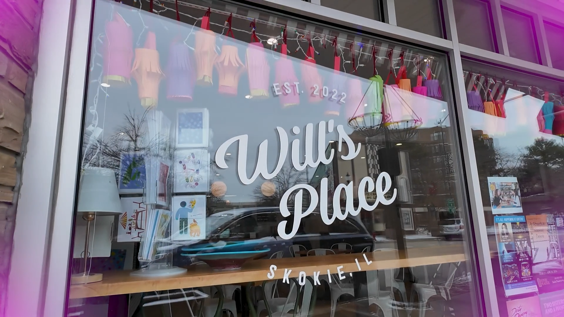 Store window with the words 'Willis Place' written on the glass, decorated with hanging paper lanterns, and various items displayed inside including artwork and lighting.