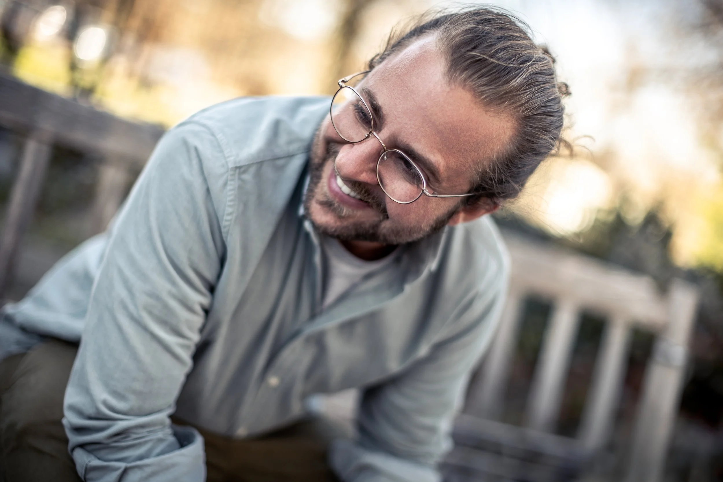 Mann mit Brille und Bart lächelt, sitzt im Freien.