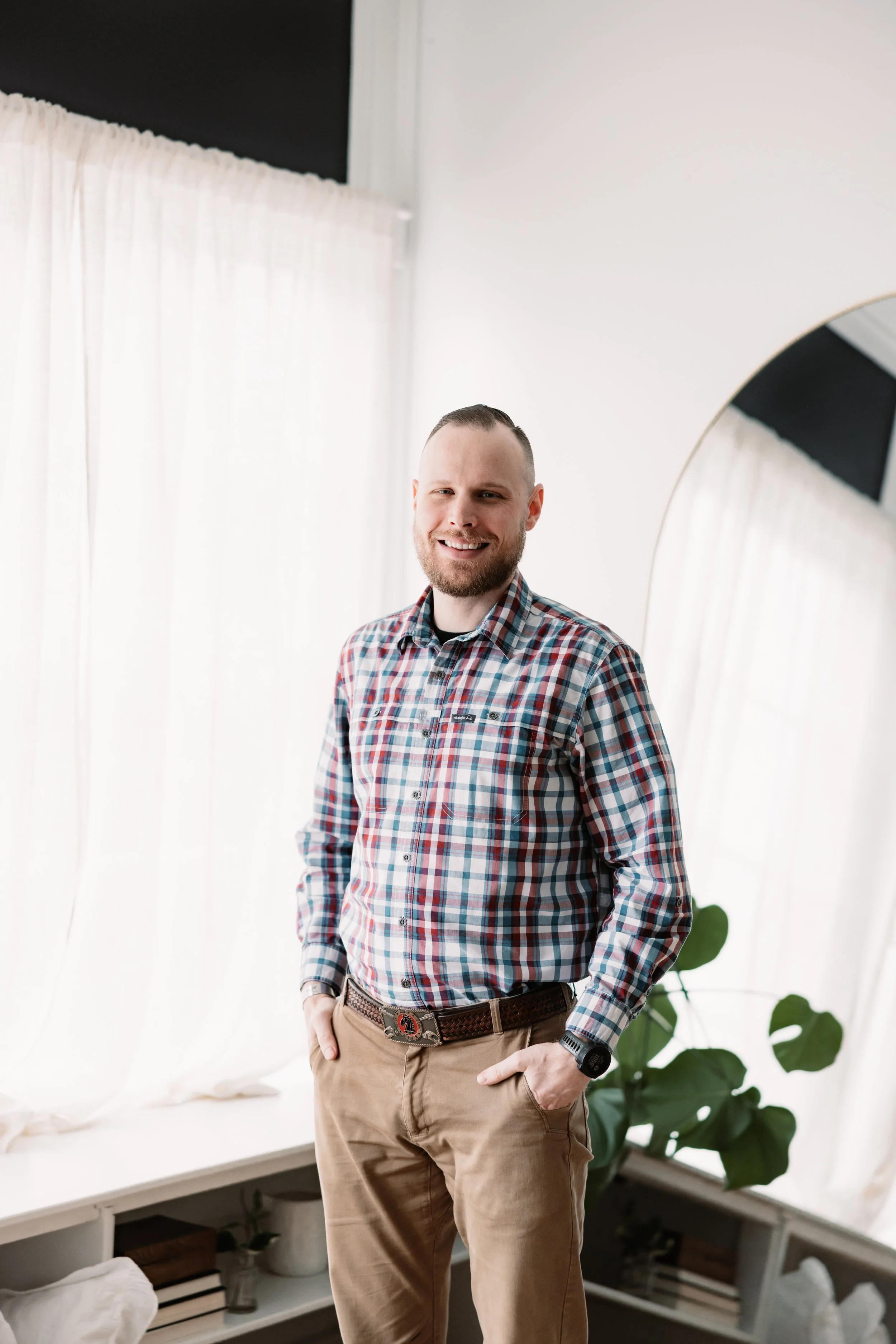 A smiling man with short light brown hair, wearing a blue Under Armour zip-up jacket and a collared shirt underneath, standing against a plain light background.