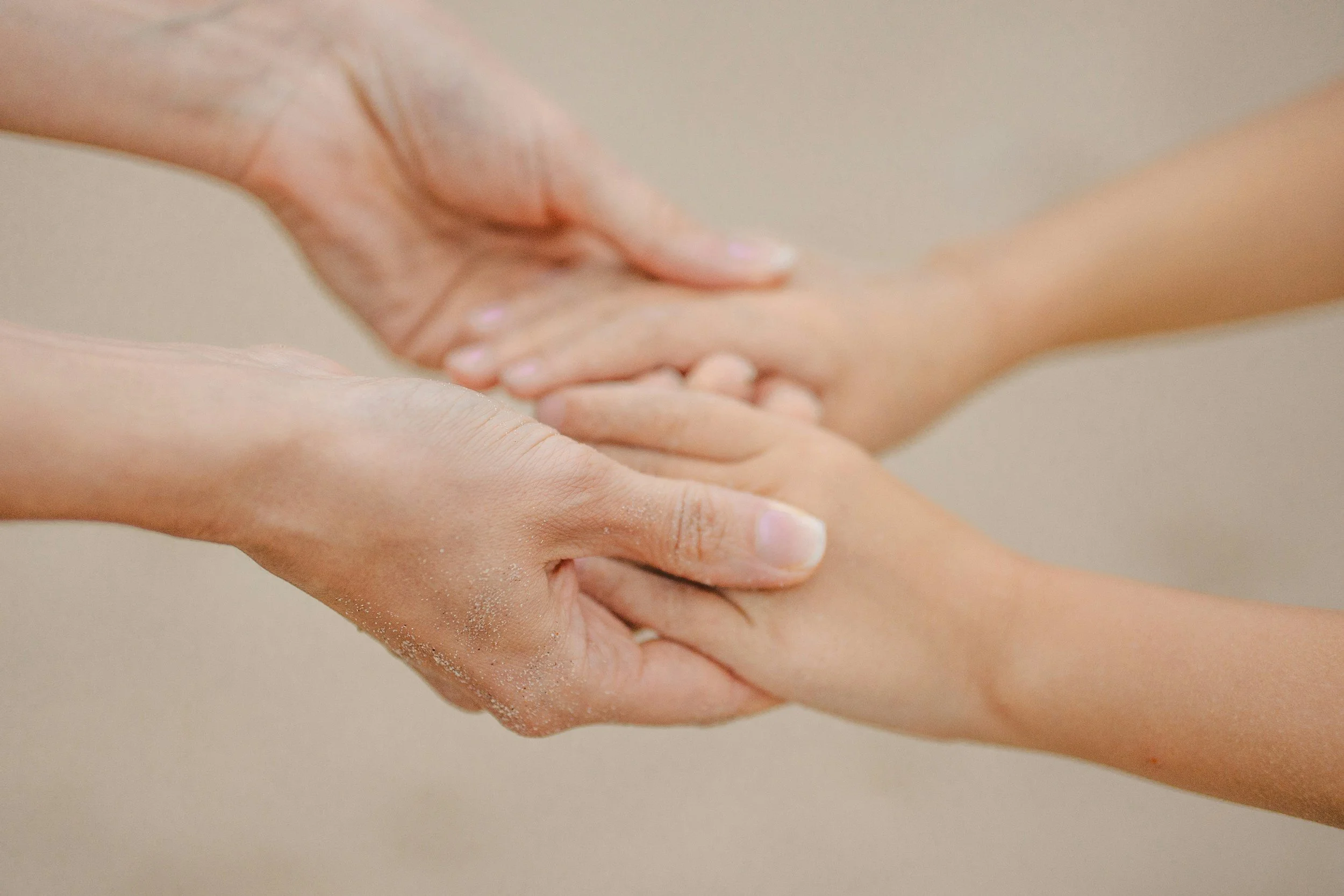 Two pairs of hands holding each other in a gentle handshake.