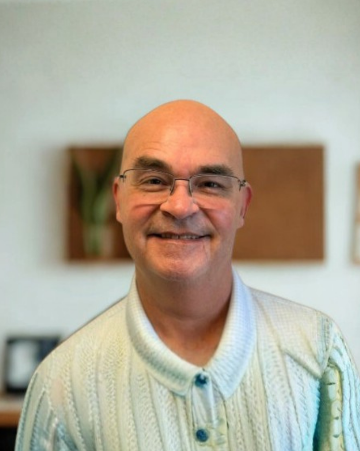 A smiling bald man wearing glasses and a light-colored collared shirt.