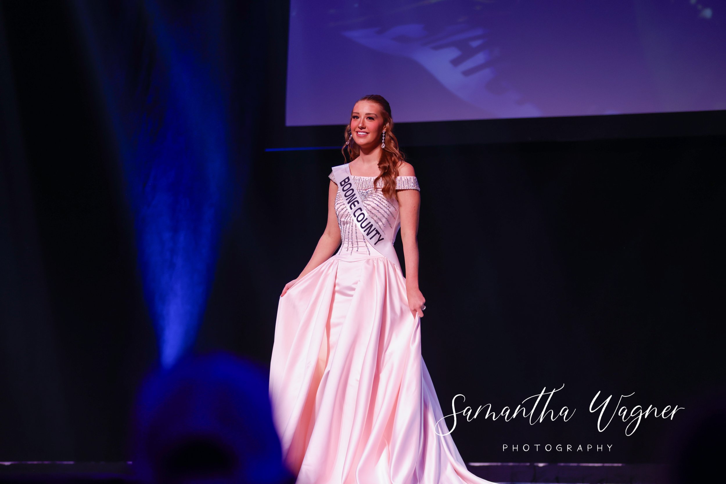 Person in an evening gown with "Boone County" sash on stage.