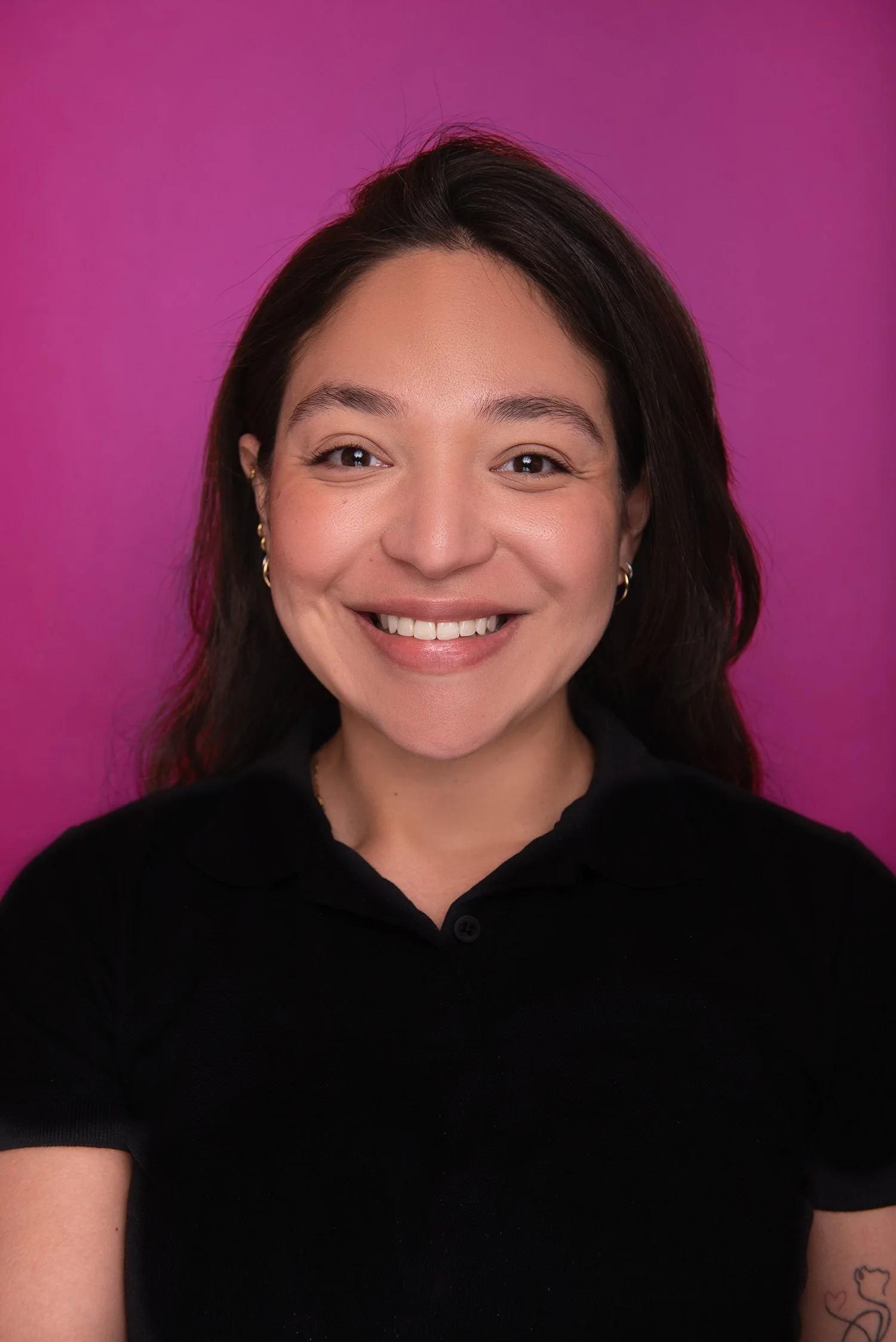 A woman with long, light brown hair smiling at the camera, wearing a black shirt, against a dark background.
