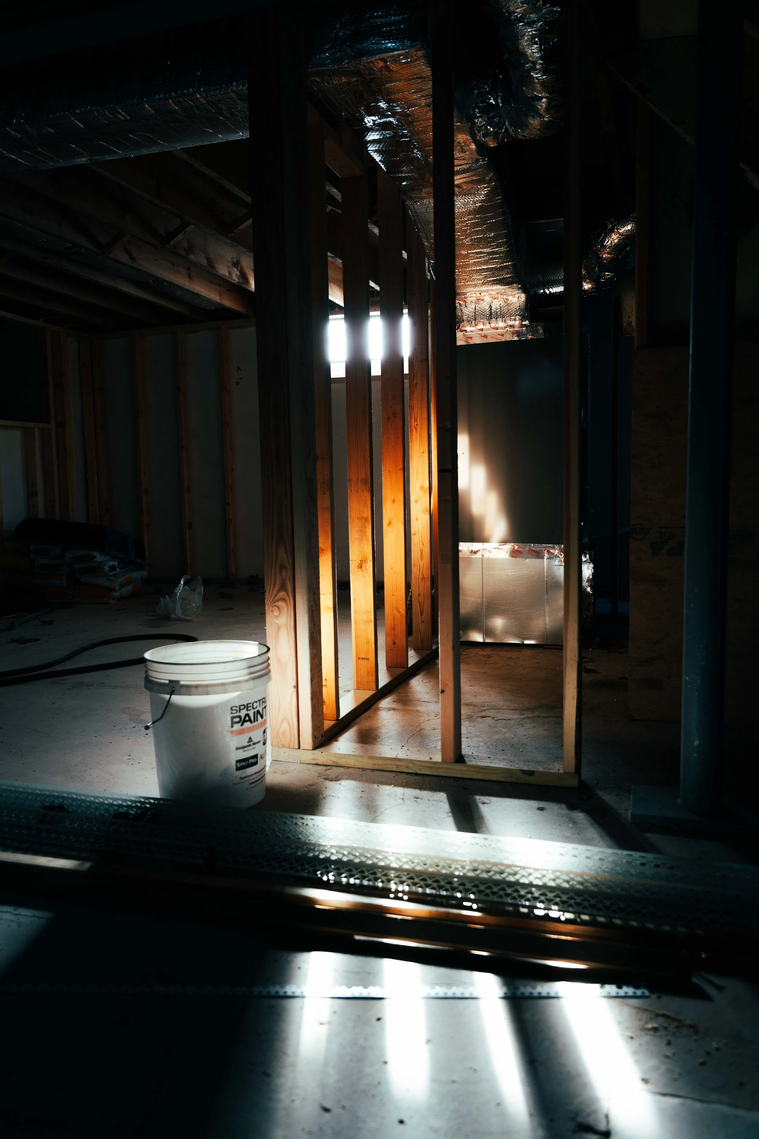 Construction site of a building with wood framing and exposed ducts, with sunlight streaming through an opening.