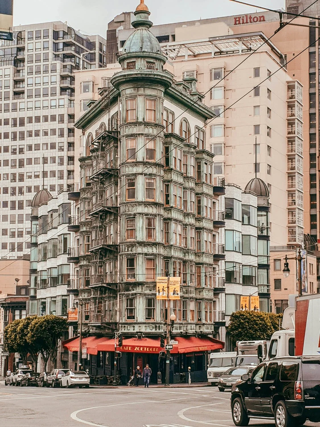 A historic, ornate, greenish Victorian-style building with many small balconies and turret towers, situated in downtown San Francisco.