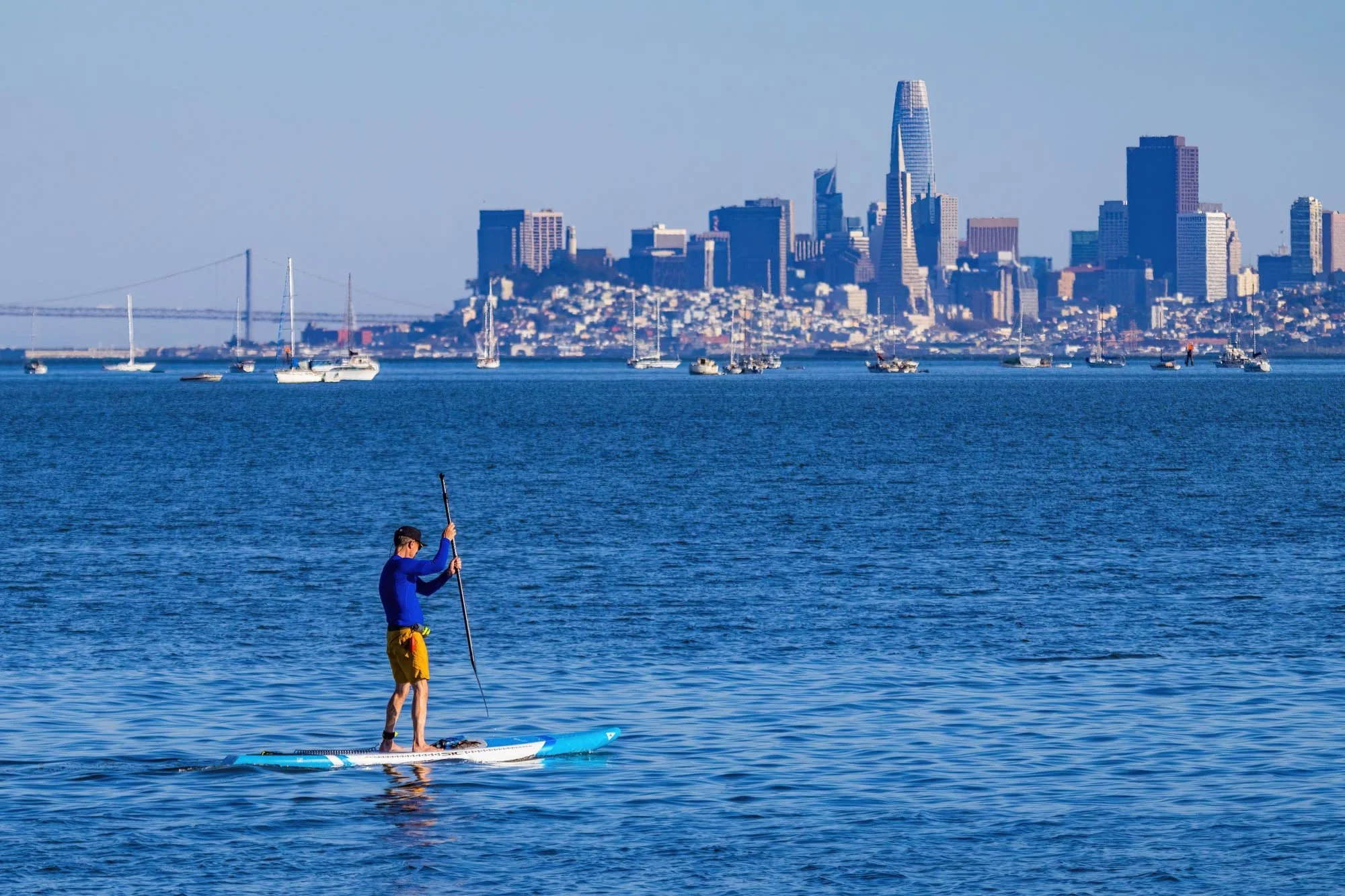 Person paddleboarding on the water with San Francisco city skyline in the background.