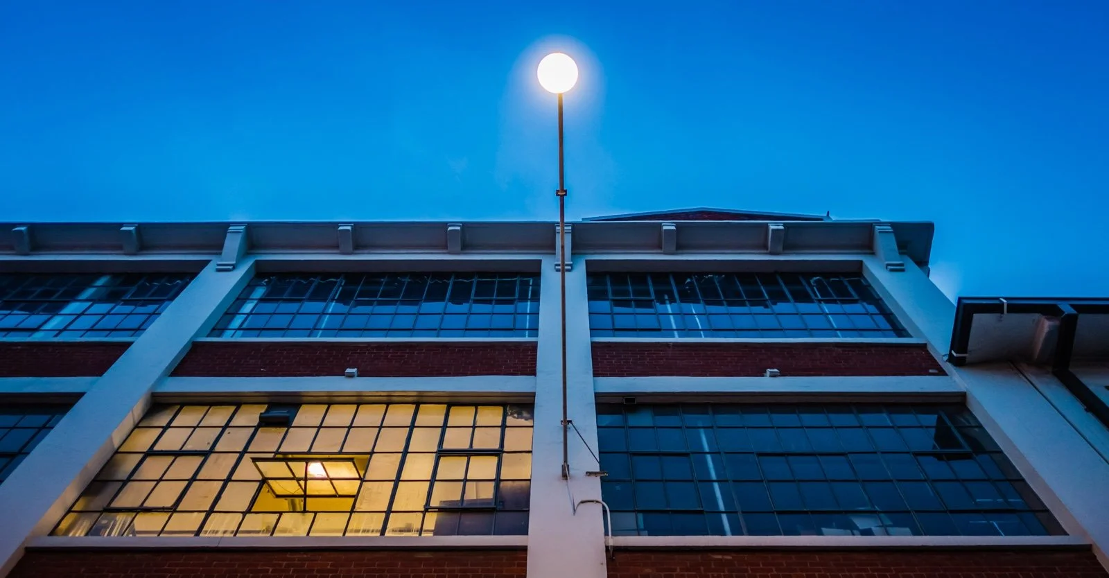 Upward view form the sidewalk of an industrial building (the American Industrial Center) at dusk, with a glowing streetlamp on