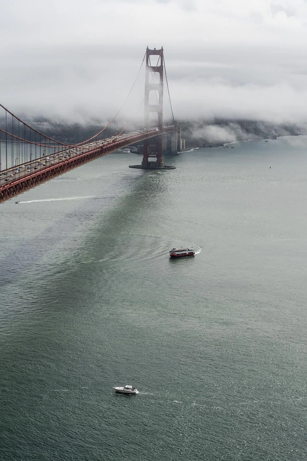 The Golden Gate Bridge partially shrouded in fog over a body of water with several boats sailing underneath.