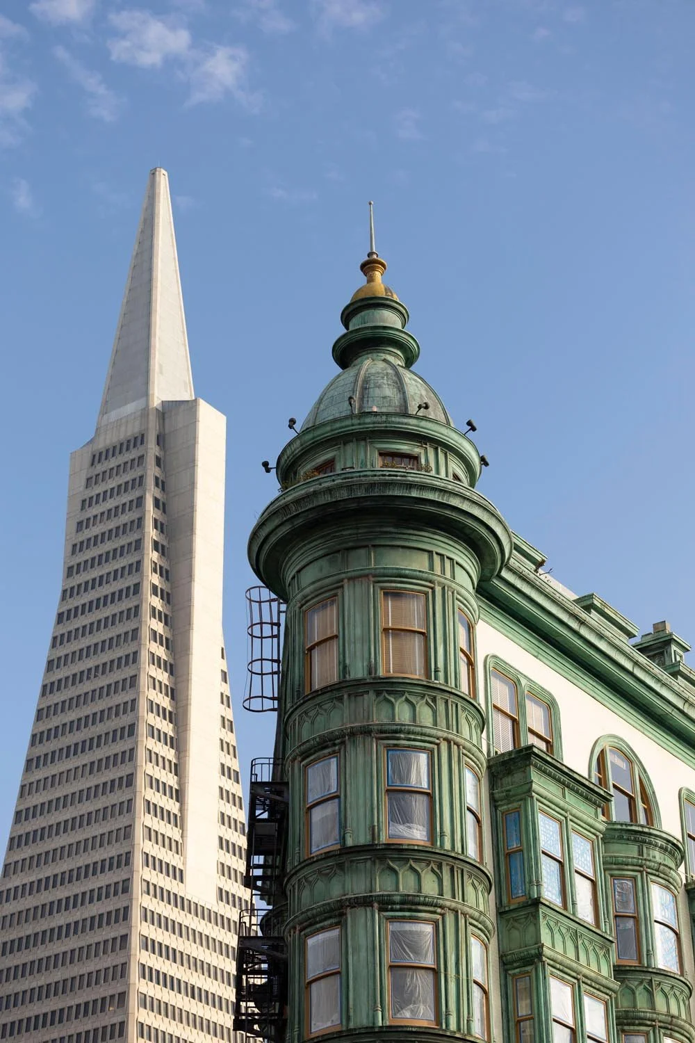 Close-up of San Francisco's old pink-painted Victorian-style building with a rounded turret, next to a modern high-rise skyscraper.