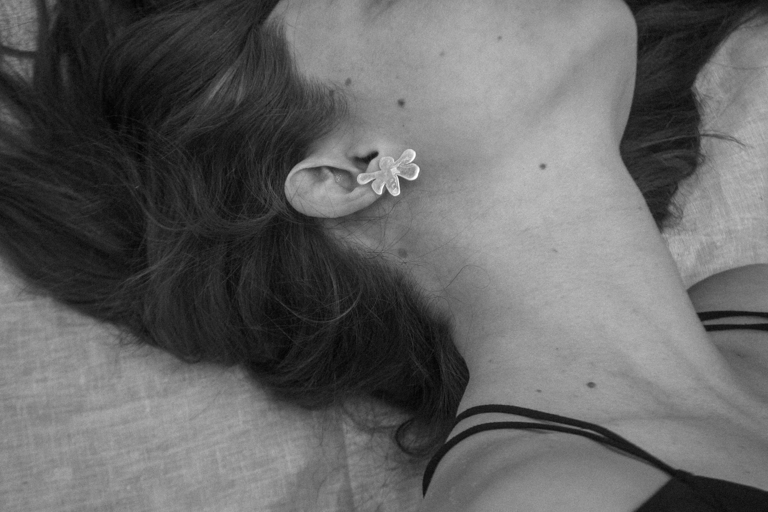 Mujer acostada de lado con una flor de goma en la oreja y cabello oscuro, vista de perfil.