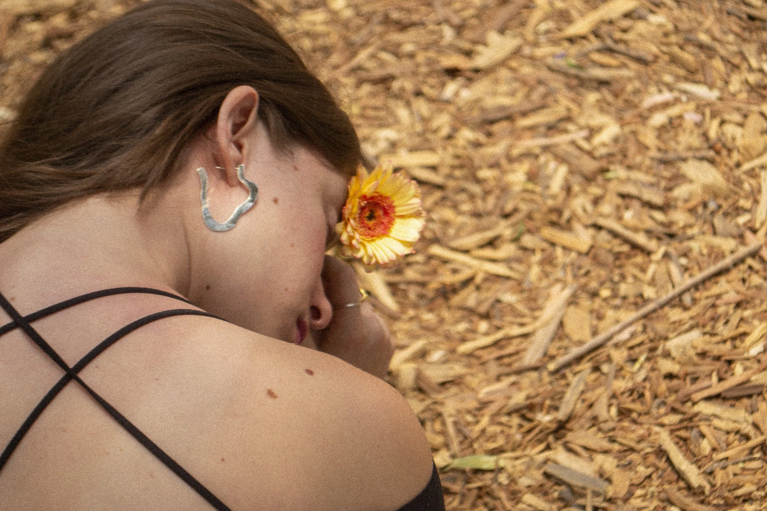 Mujer con pez en la oreja, arrodillada en un suelo de madera, con flor en la cara y ropa de tirantes.