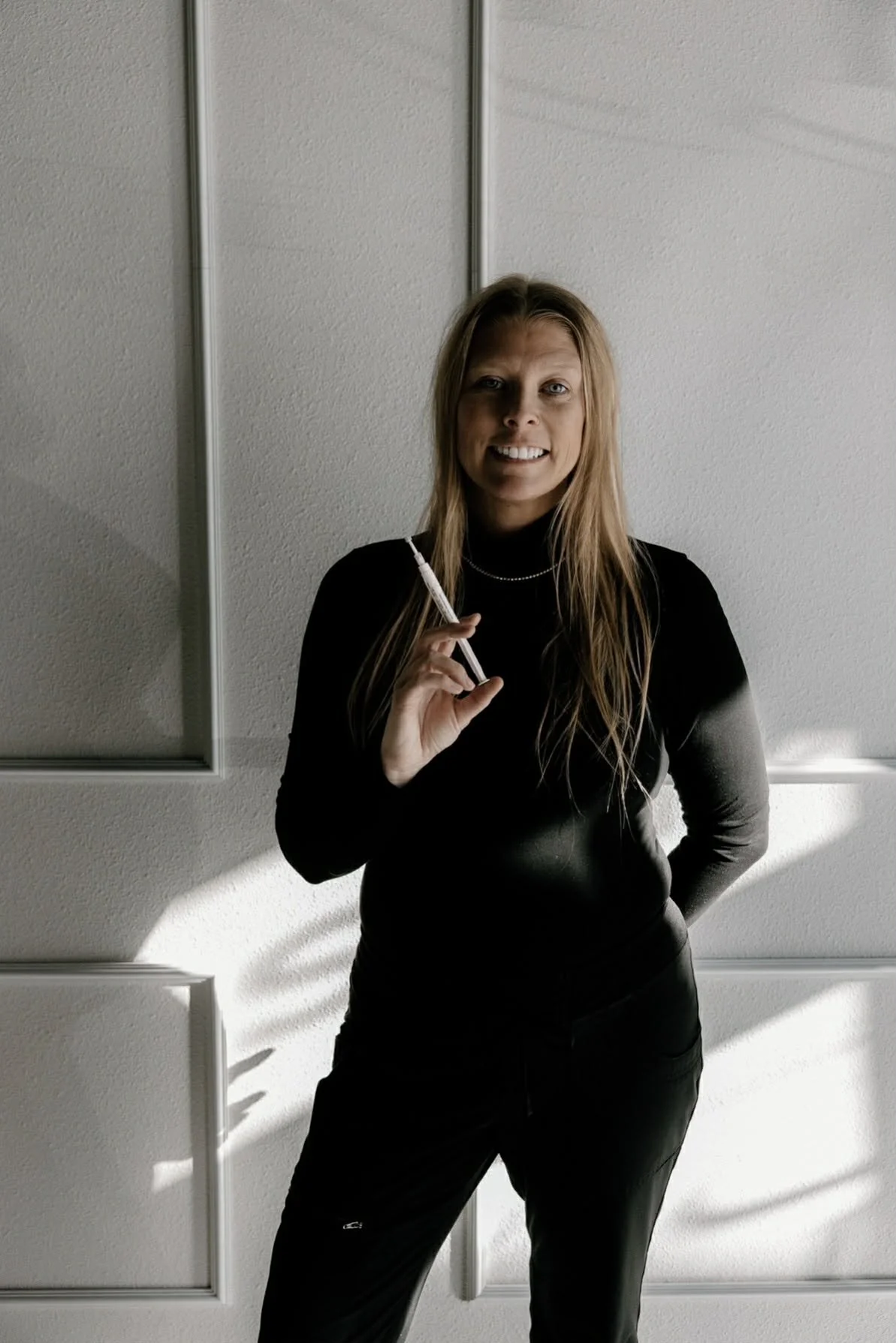 Owner of LUXE Whitening Lounge smiling and holding a teeth whtiening syringe, welcoming clients to a luxury teeth-whitening experience.