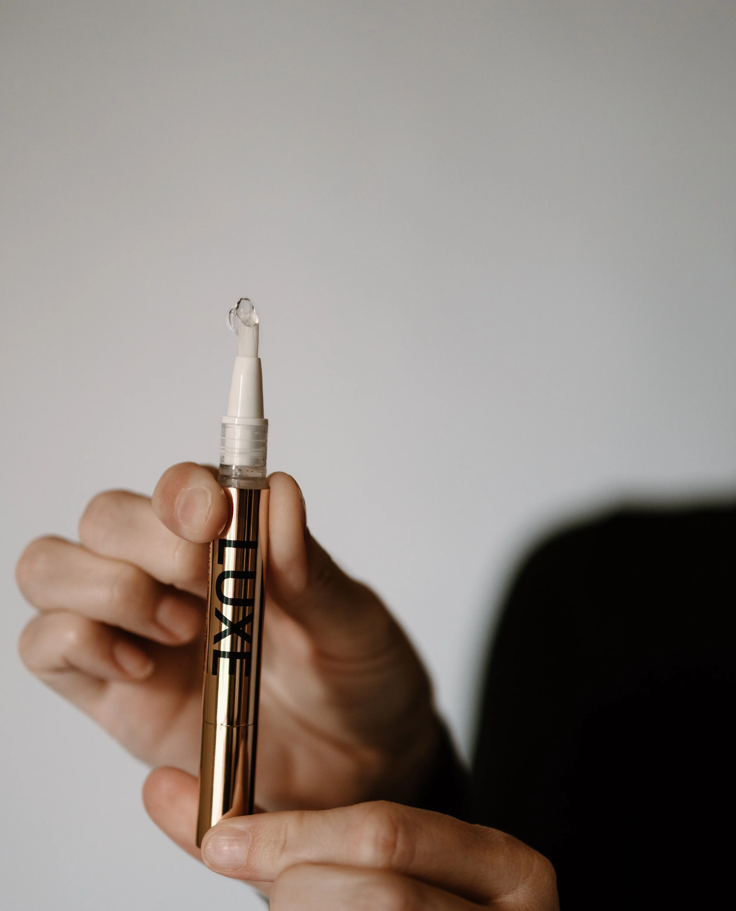 A hand holding a gold-colored pen with the word LUXE written on it, against a plain white background.