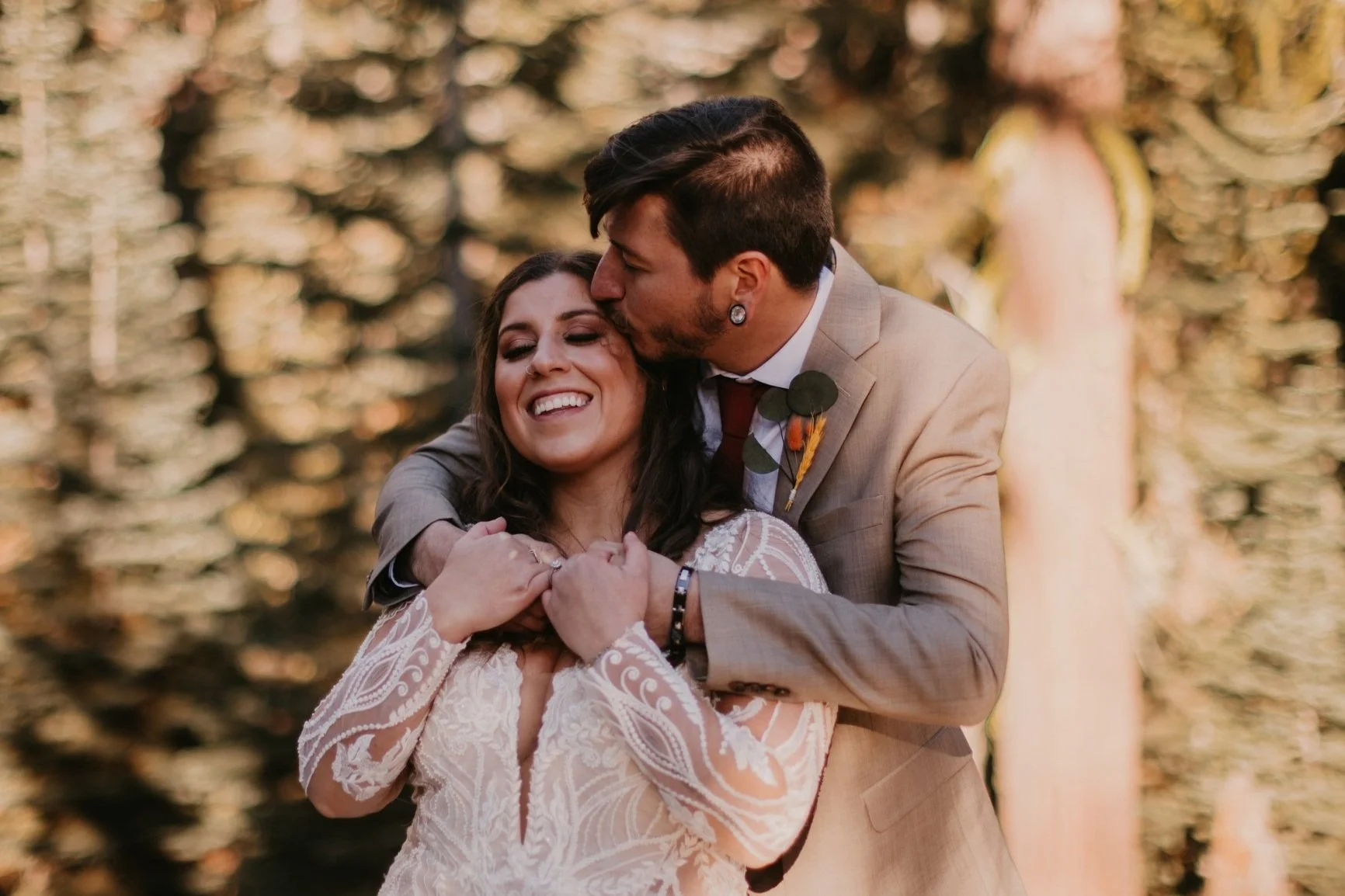 Groom kissing bride on head during wedding in wooded clearing in Yosemite National Park.