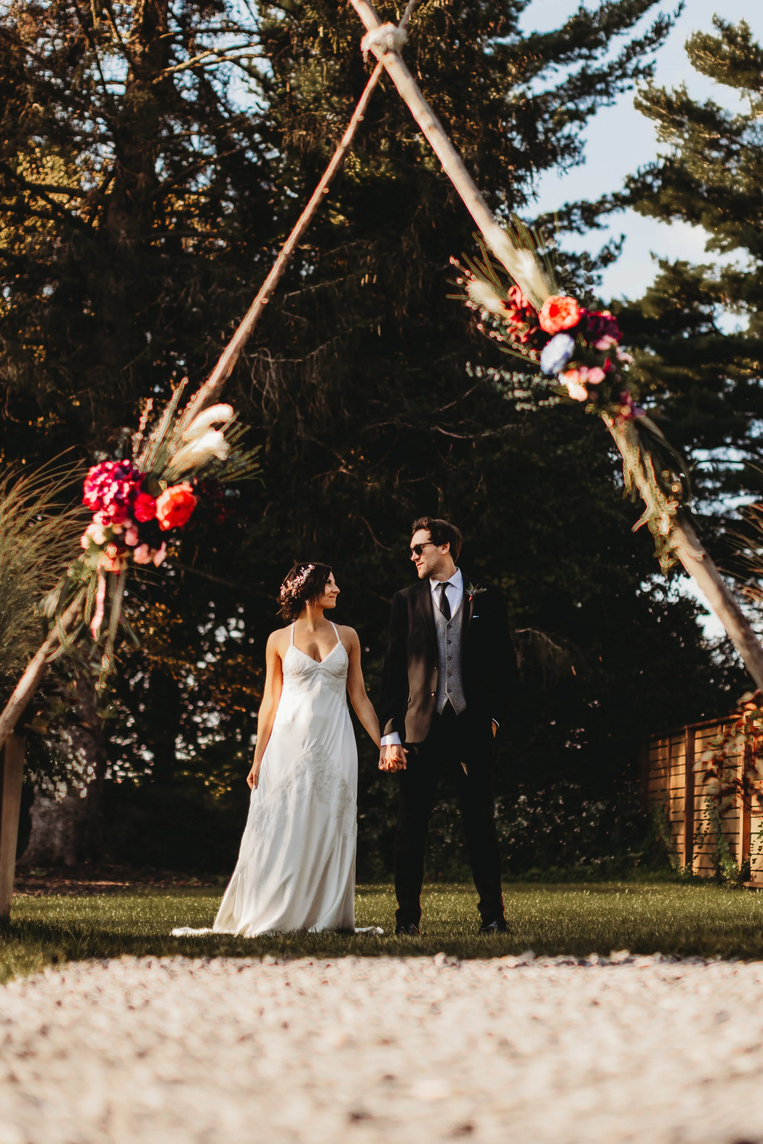 Sunset Wedding ceremony in Skaneateles New York. Couple holding hands under florals.