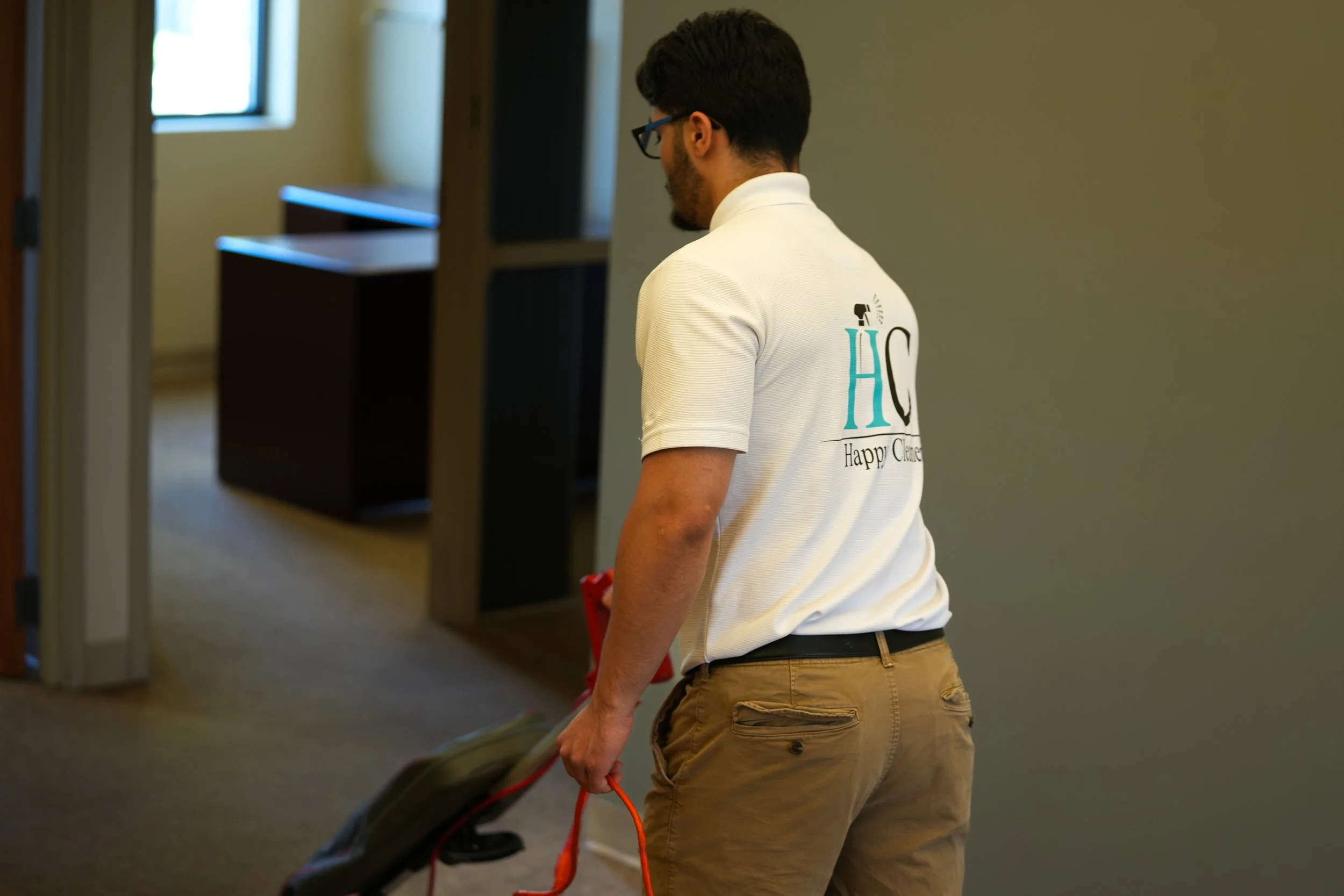 A man wearing glasses and a white polo shirt walking through an indoor space, pulling a stroller.