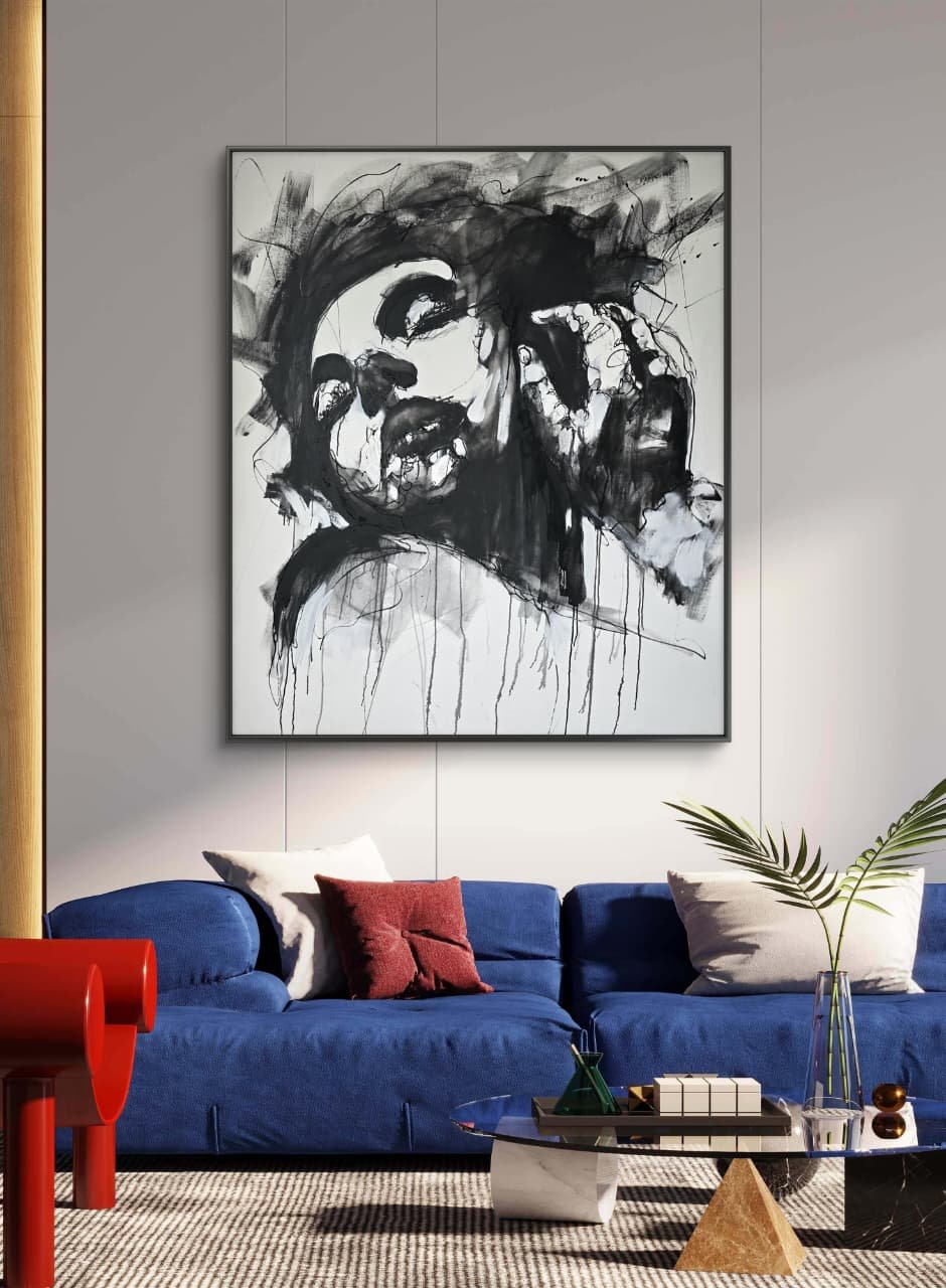 Living room with a large framed black and white abstract portrait on the wall, a blue sofa with white and red pillows, a glass coffee table with decorative items, a green glass bottle with a large plant, a red side table, and a beige rug.